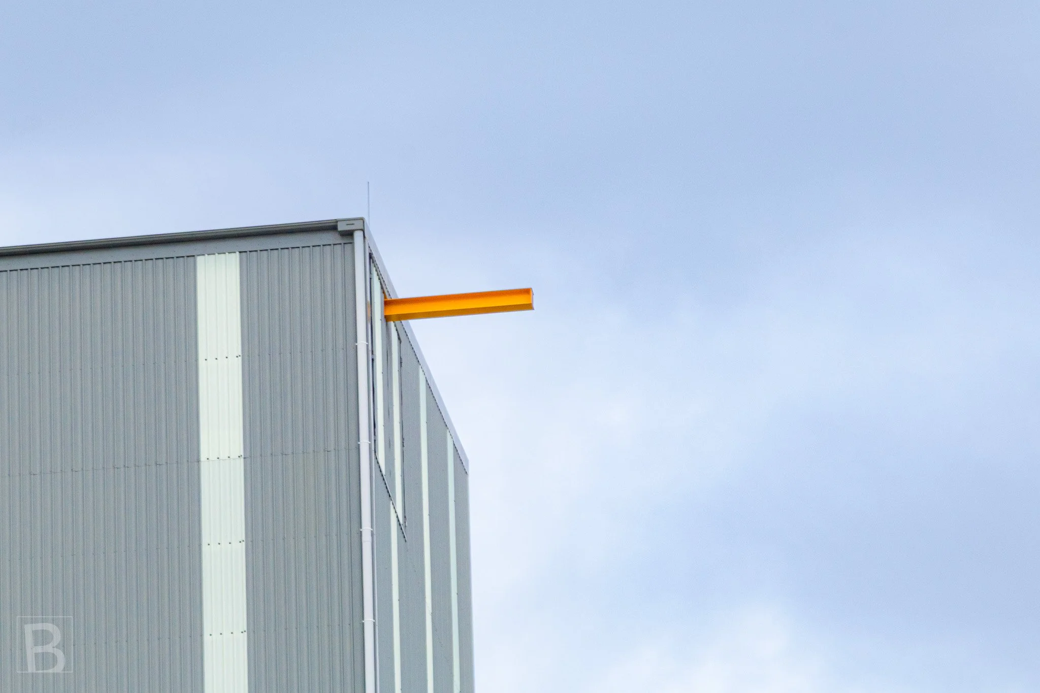 An isolated orange structural element adds tension and colour to the
clean vertical lines of an industrial facade.
