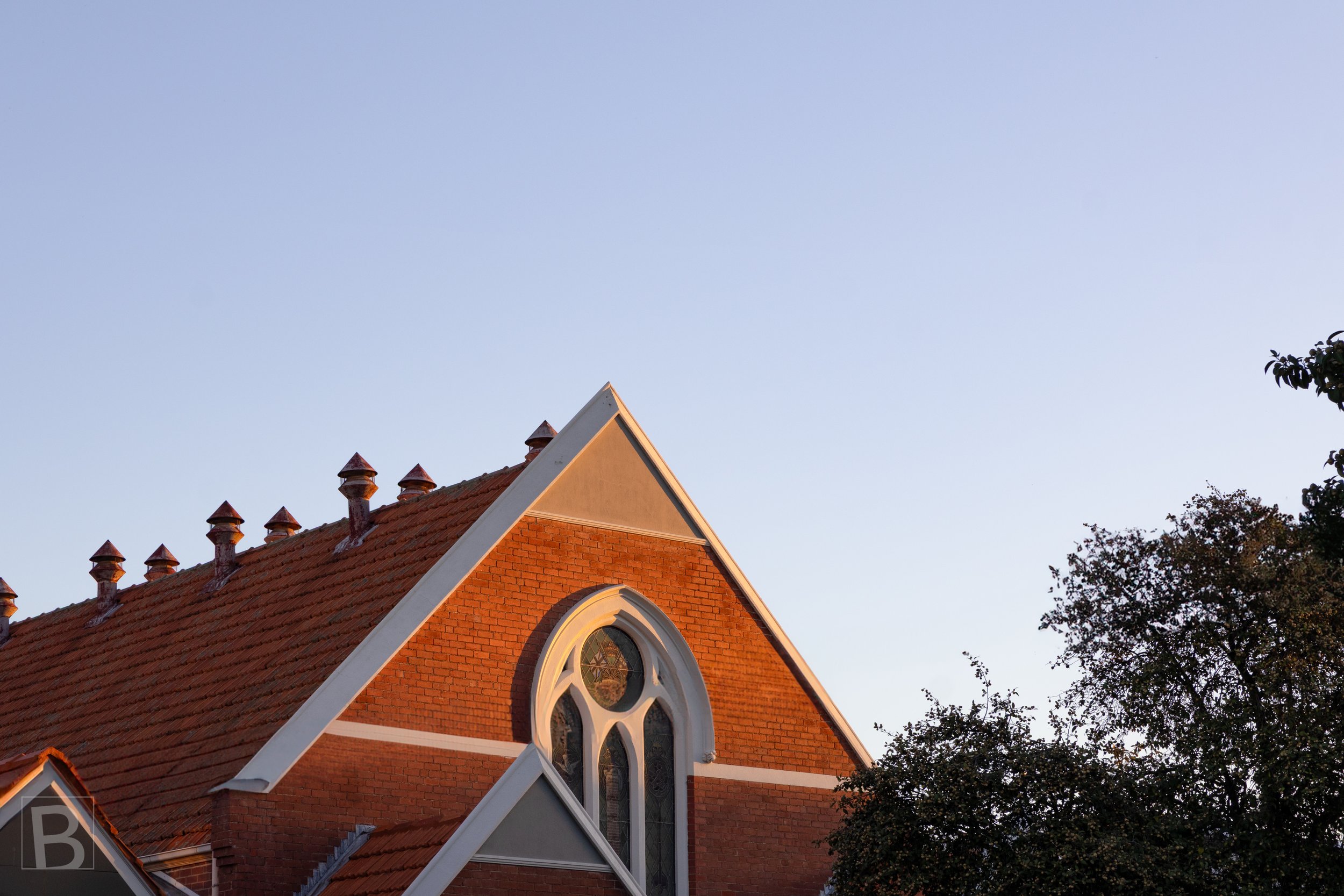 Warm brick, patterned roof tiles and Gothic details emerge quietly
against the fading evening sky.