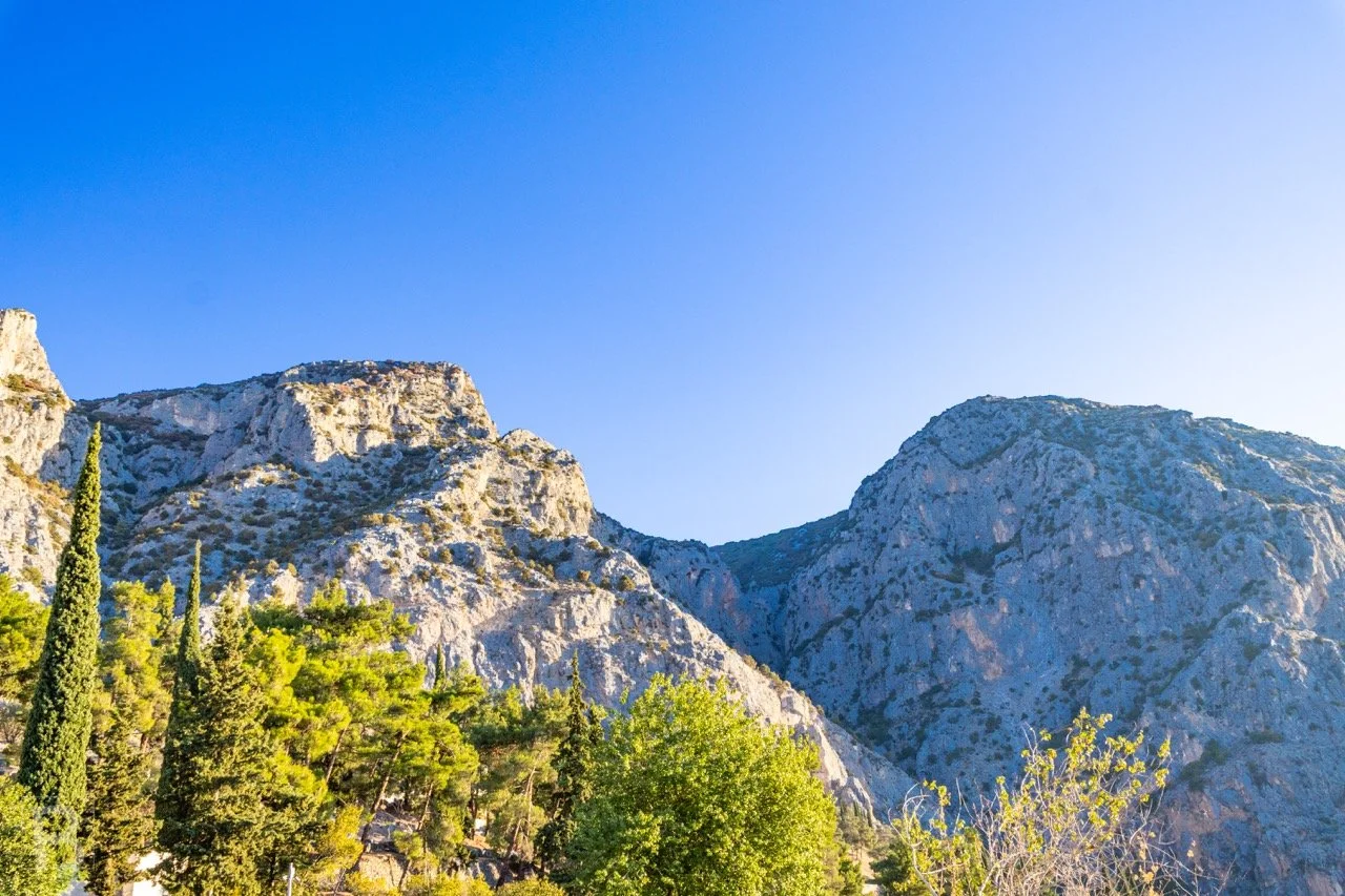 Crisp daylight reveals the pale texture of a rocky mountain range
above trees, creating a bold study of stone, colour and open sky. At the oracle of Delphi