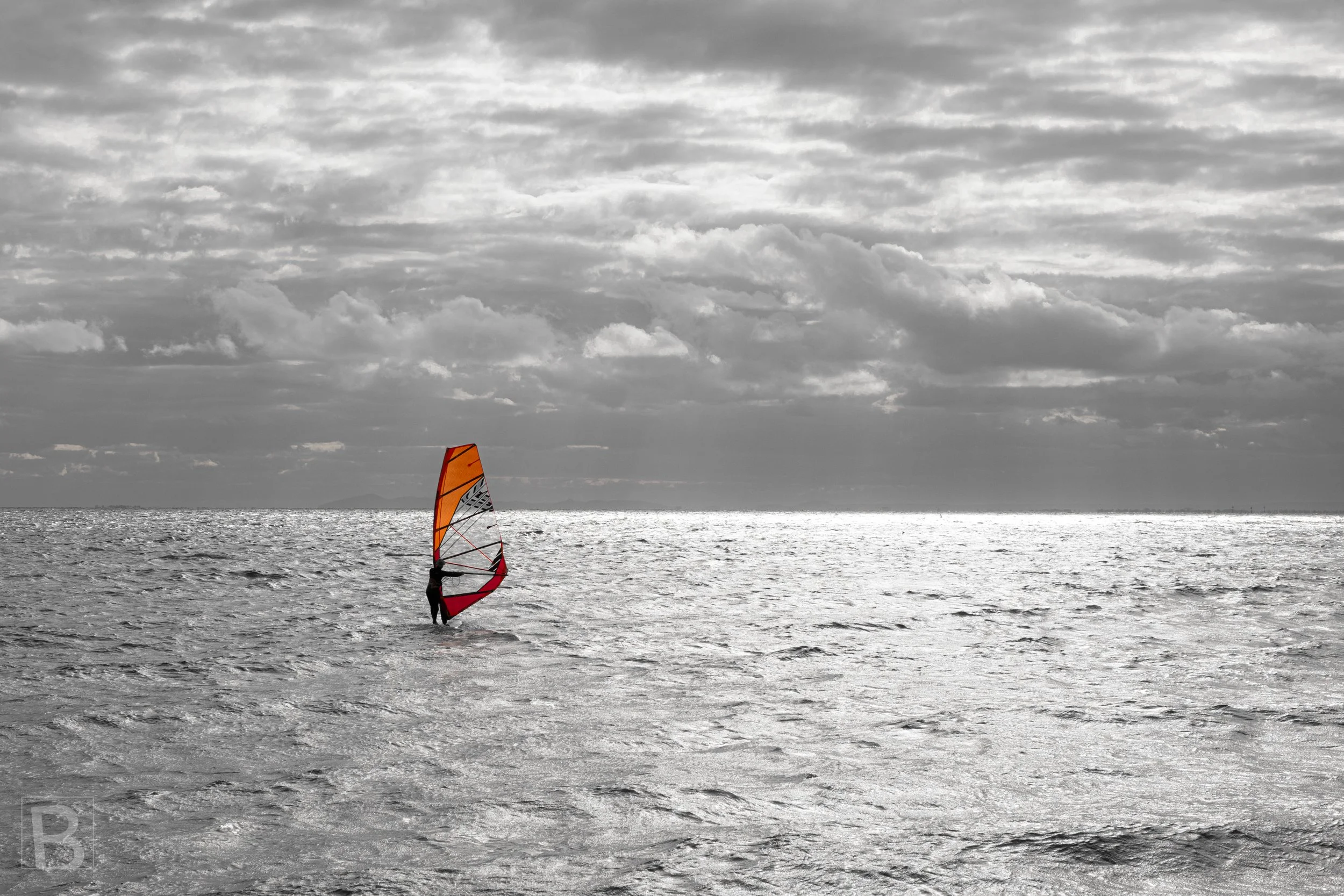 A bright windsurfing sail punctuates a restrained seascape, bringing a
flash of colour to water and cloud.