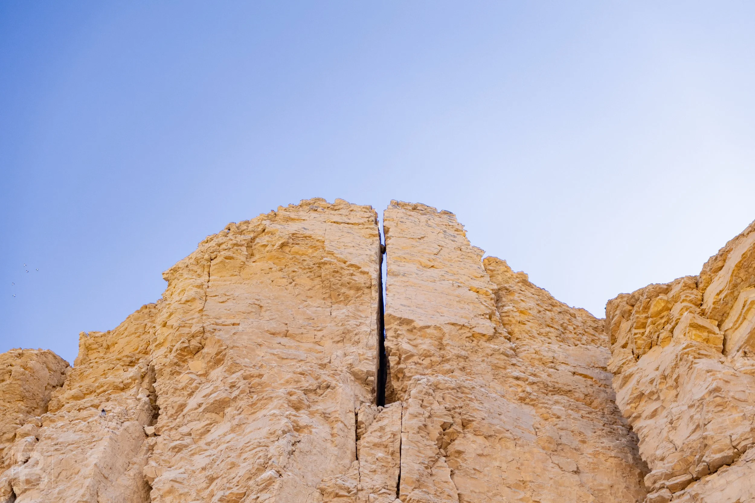 A deep split through weathered stone at the valley of the kings Egypt creates a striking natural
geometry, framed against an uninterrupted blue sky.