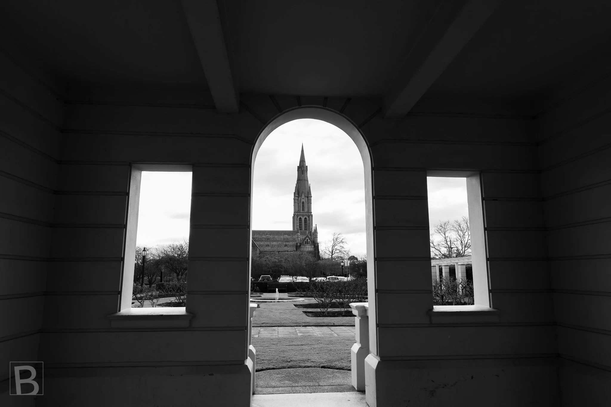 Black and white photograph looking through a dark interior towards an arched doorway and the Brighton civic precinct beyond.