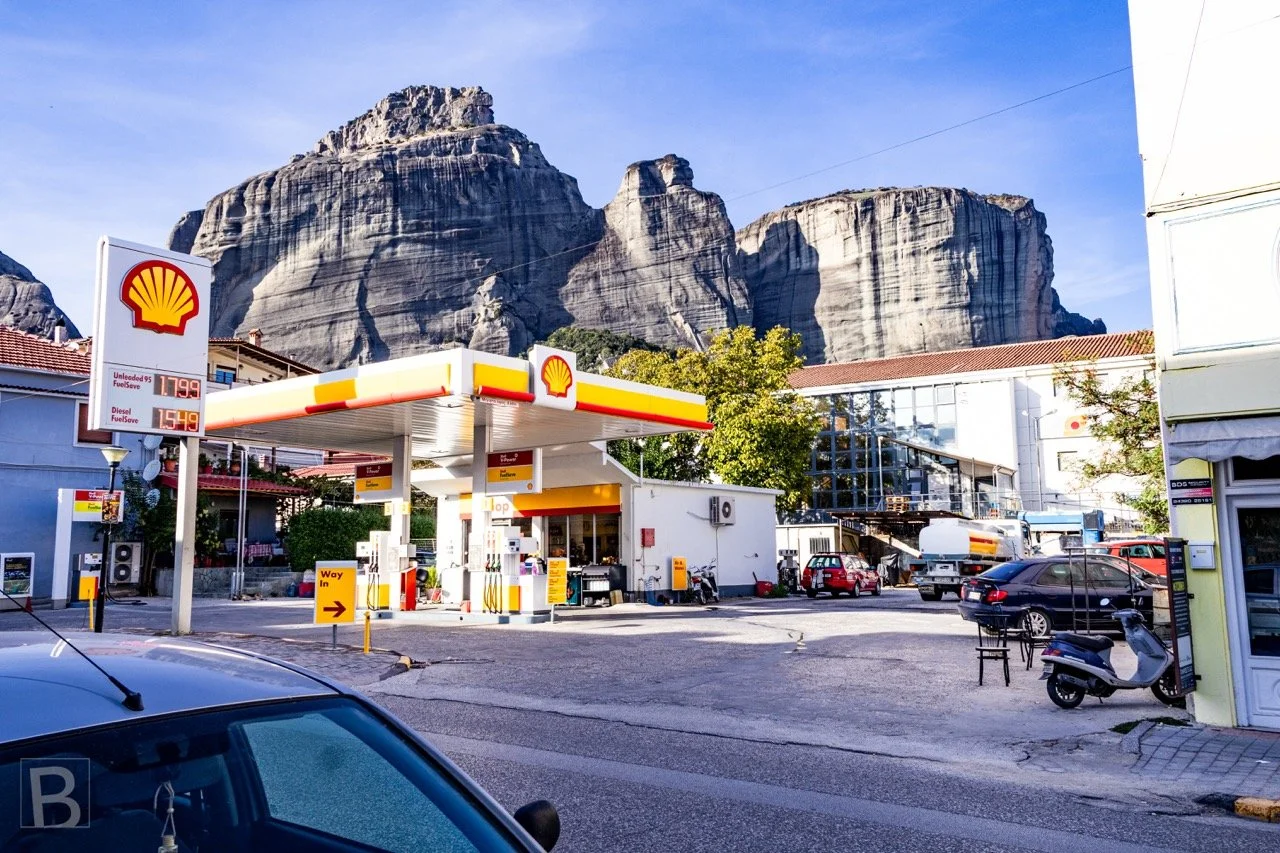 The monumental cliffs of Meteora appear beyond a familiar roadside
petrol station, bringing the extraordinary into an ordinary urban
moment.