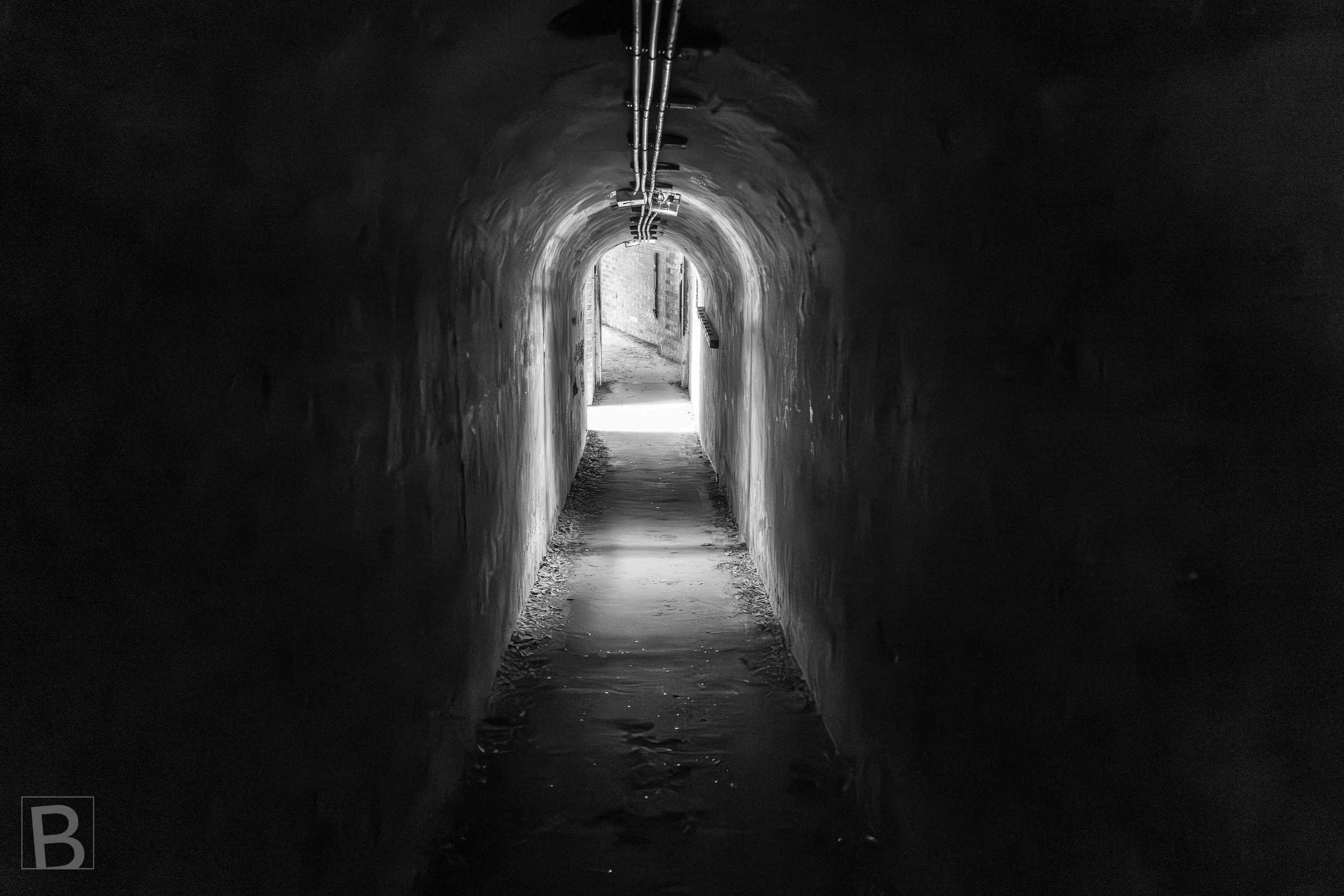 Light at the end of a confined historic passage reveals worn surfaces,
old services and the accumulated texture of use.