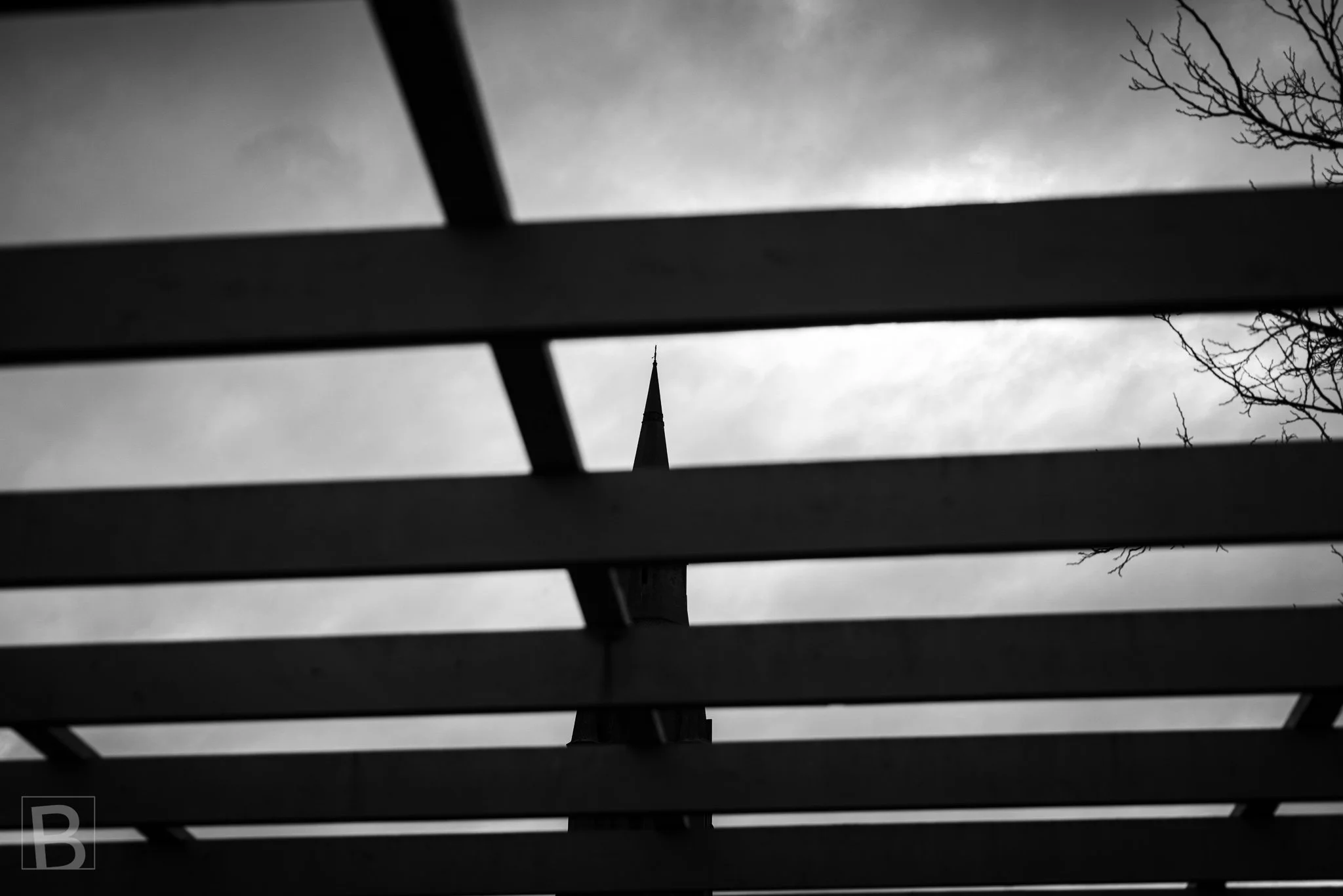 Black and white photograph looking upward through a series of dark structural beams against a cloudy sky in Brighton, Melbourne.