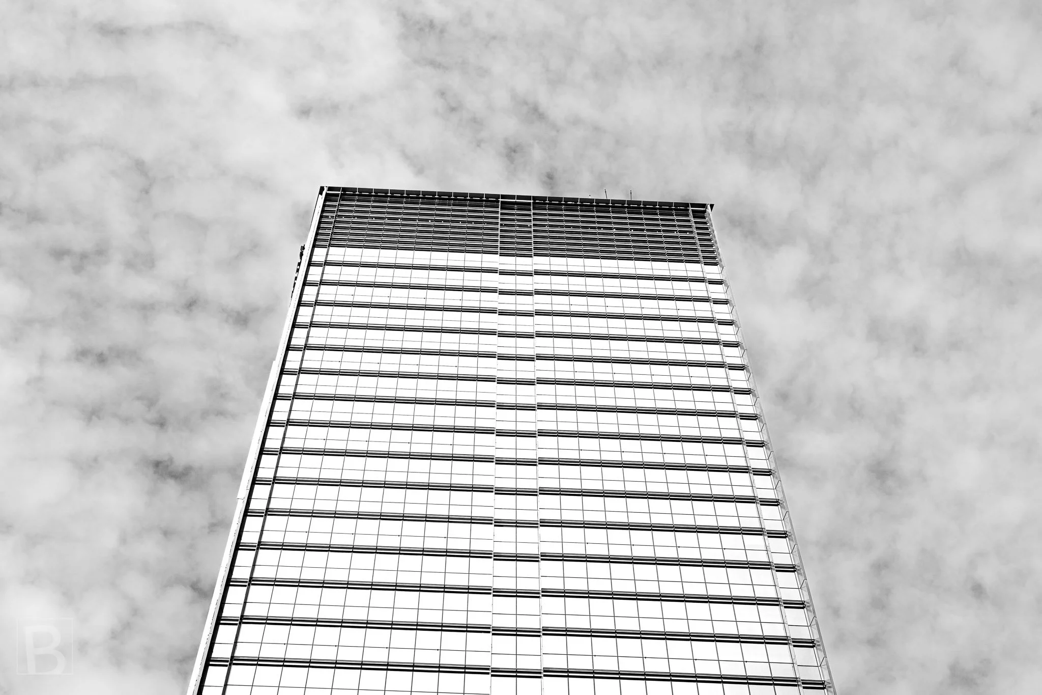 Fine horizontal bands repeat across a restrained office tower,
emphasizing proportion, height and the changing cloud above.