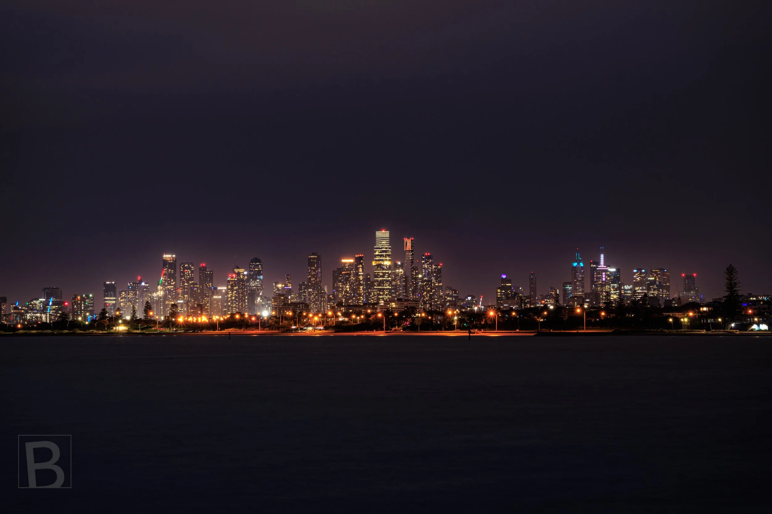 Melbourne city skyline illuminated at night, viewed across Port Phillip Bay from Brighton, Victoria.