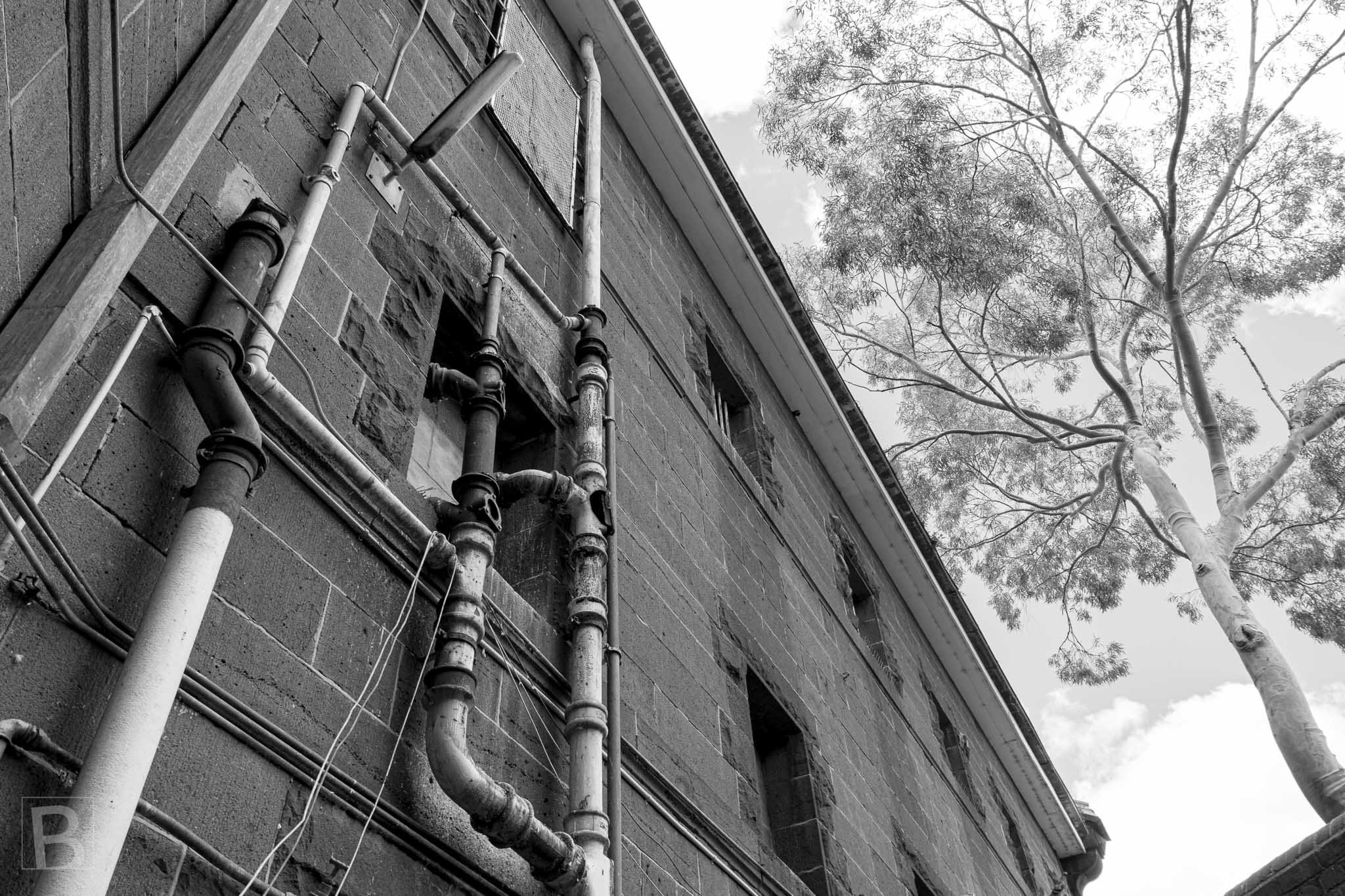 Functional pipework becomes an architectural drawing across old
brick, recording the practical layers added to a heritage building.