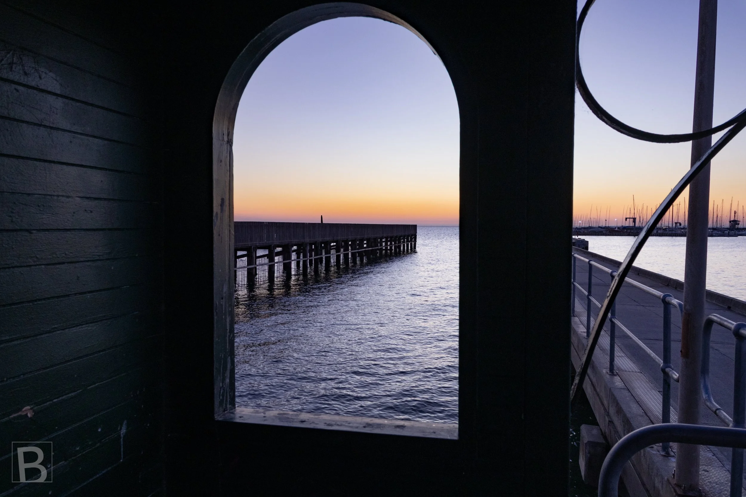 An arched opening and spiral rail frame the fading horizon,
transforming a functional pier structure into a quiet coastal
composition.