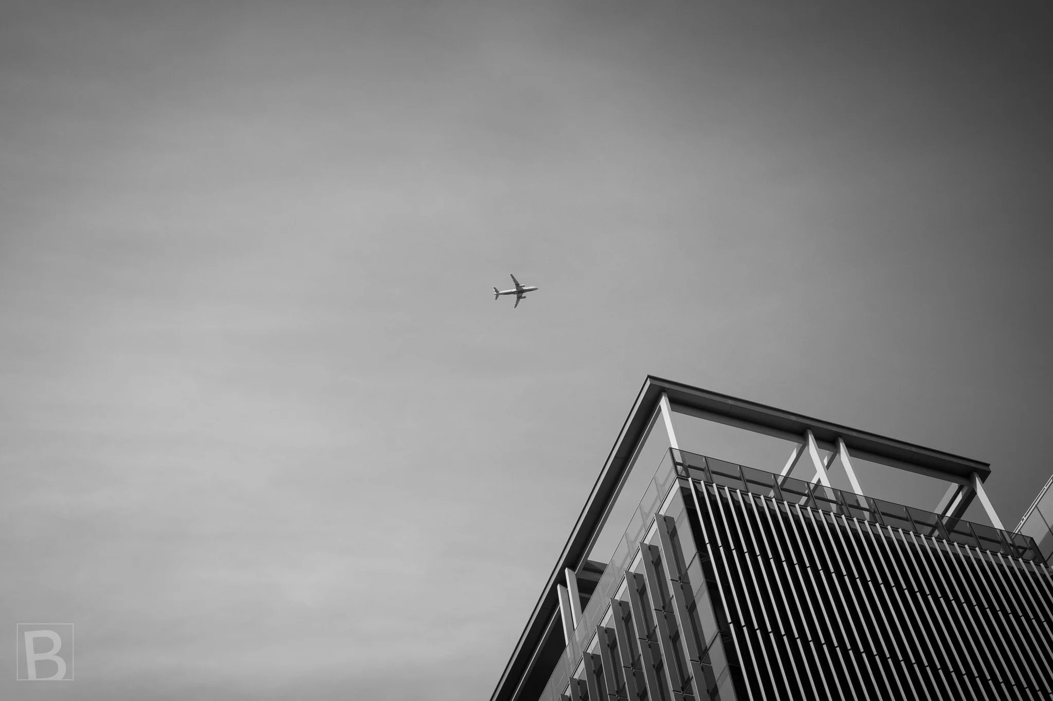 A small plane and an angular roof share a broad field of cloud,
reducing city and movement to a sparse graphic encounter.