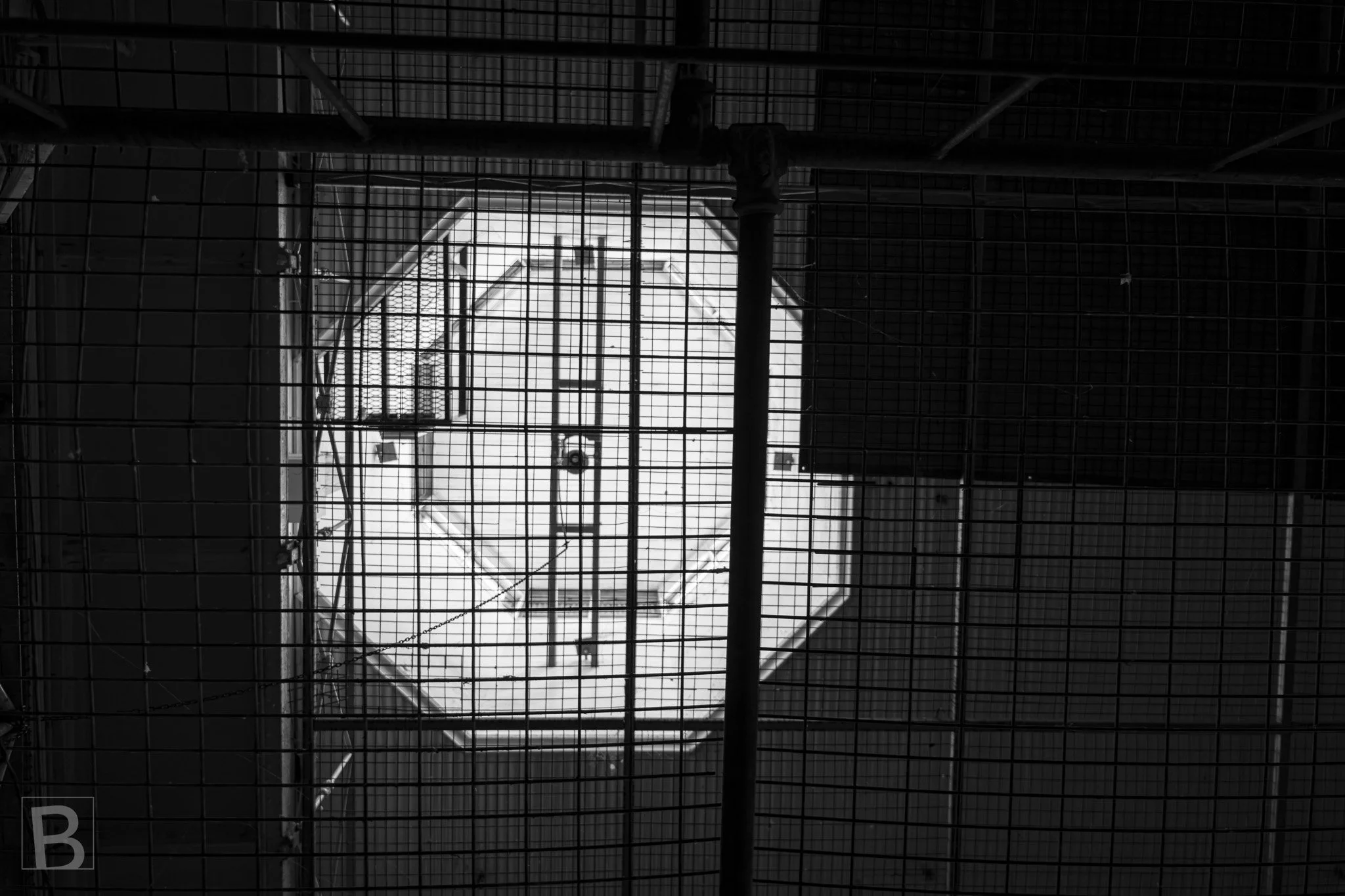 Repeated grids frame a distant opening, turning a confined utilitarian
passage into a study of depth, light and enclosure.