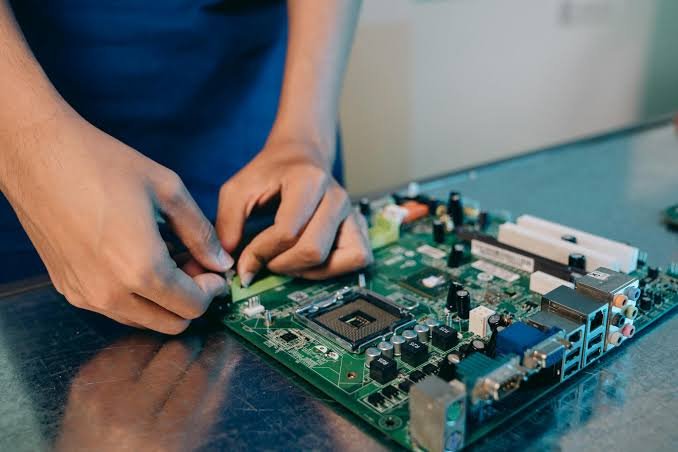 Person assembling a green computer motherboard on a black surface.