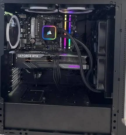 Inside a gaming PC case with a graphics card, motherboard, CPU cooler, RAM with RGB lighting, and black wiring.