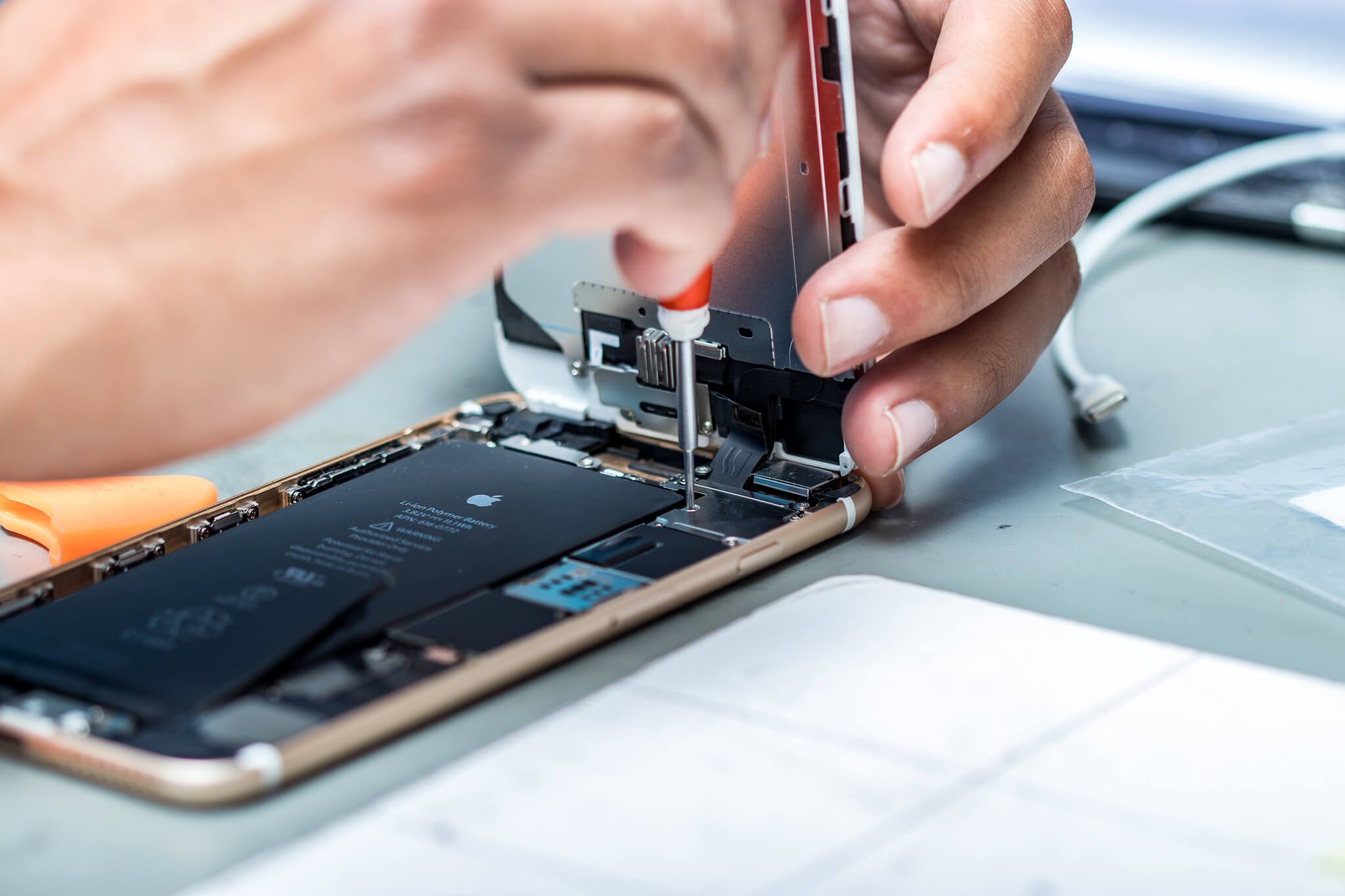 Person repairing a smartphone with a screwdriver on a workbench.