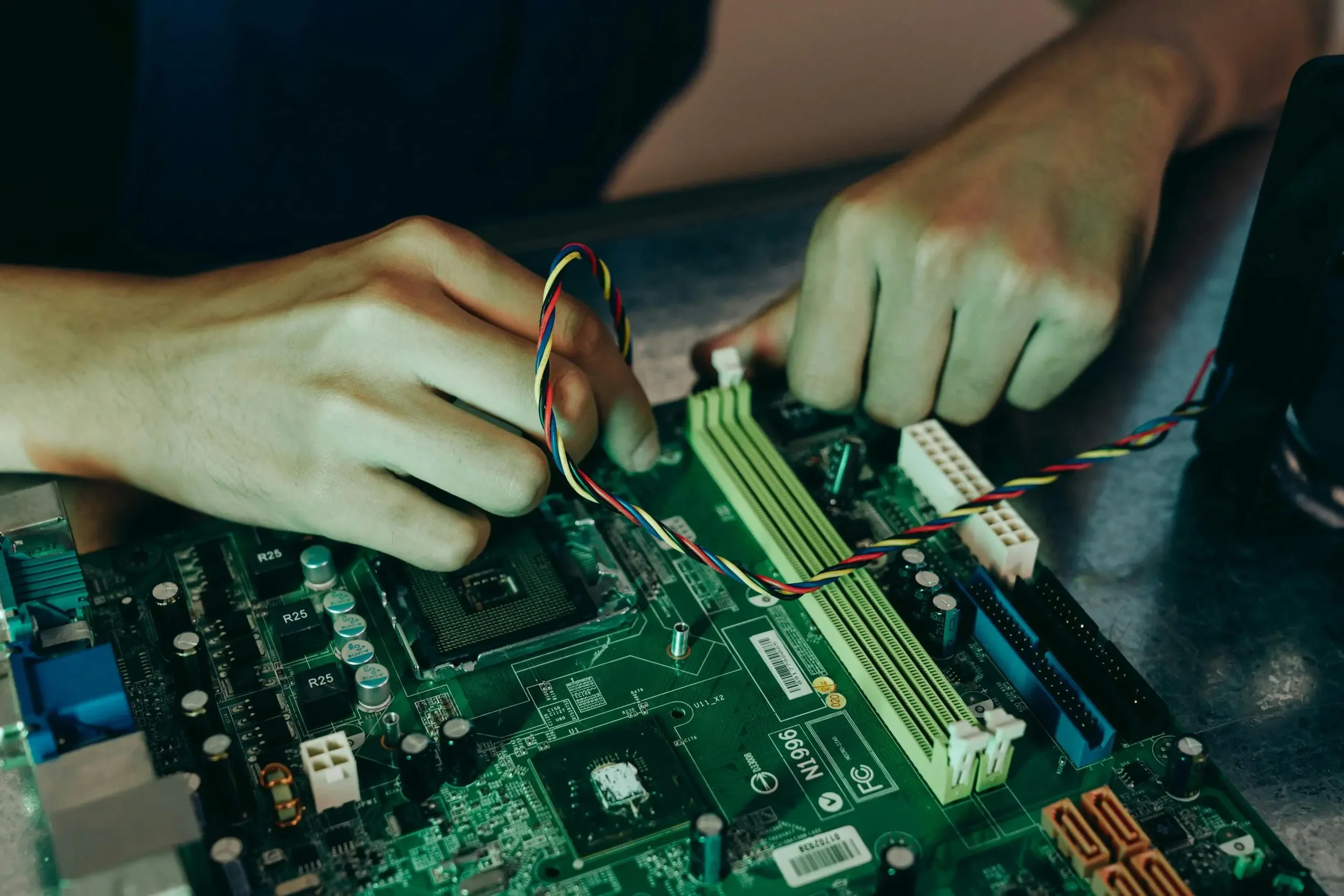 Close-up of hands installing or repairing a computer motherboard with colored wires connected.
