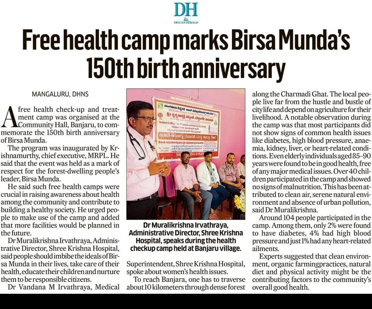 Image of Dr. Muralikrishna Irvathraya speaking at a health checklist camp in Banjaru village, with a poster in the background and seated attendees.