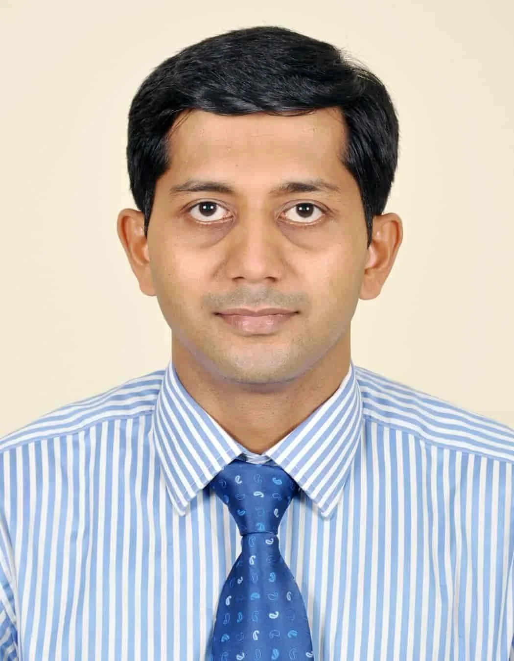 Professional headshot of a man with black hair, wearing a blue and white striped shirt and blue tie, against a plain beige background.