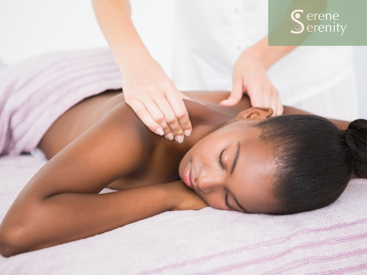 A woman receives a massage on her shoulder from a massage therapist in a spa setting with a towel covering her lower body.