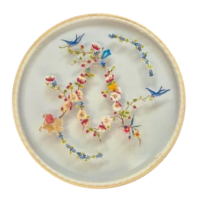 Decorative round plate with embroidered floral design and two bluebirds.