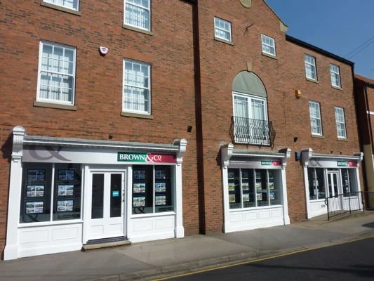Real estate agency with 'Brown QC' sign on the storefront, located on a brick building with multiple windows and a small balcony.