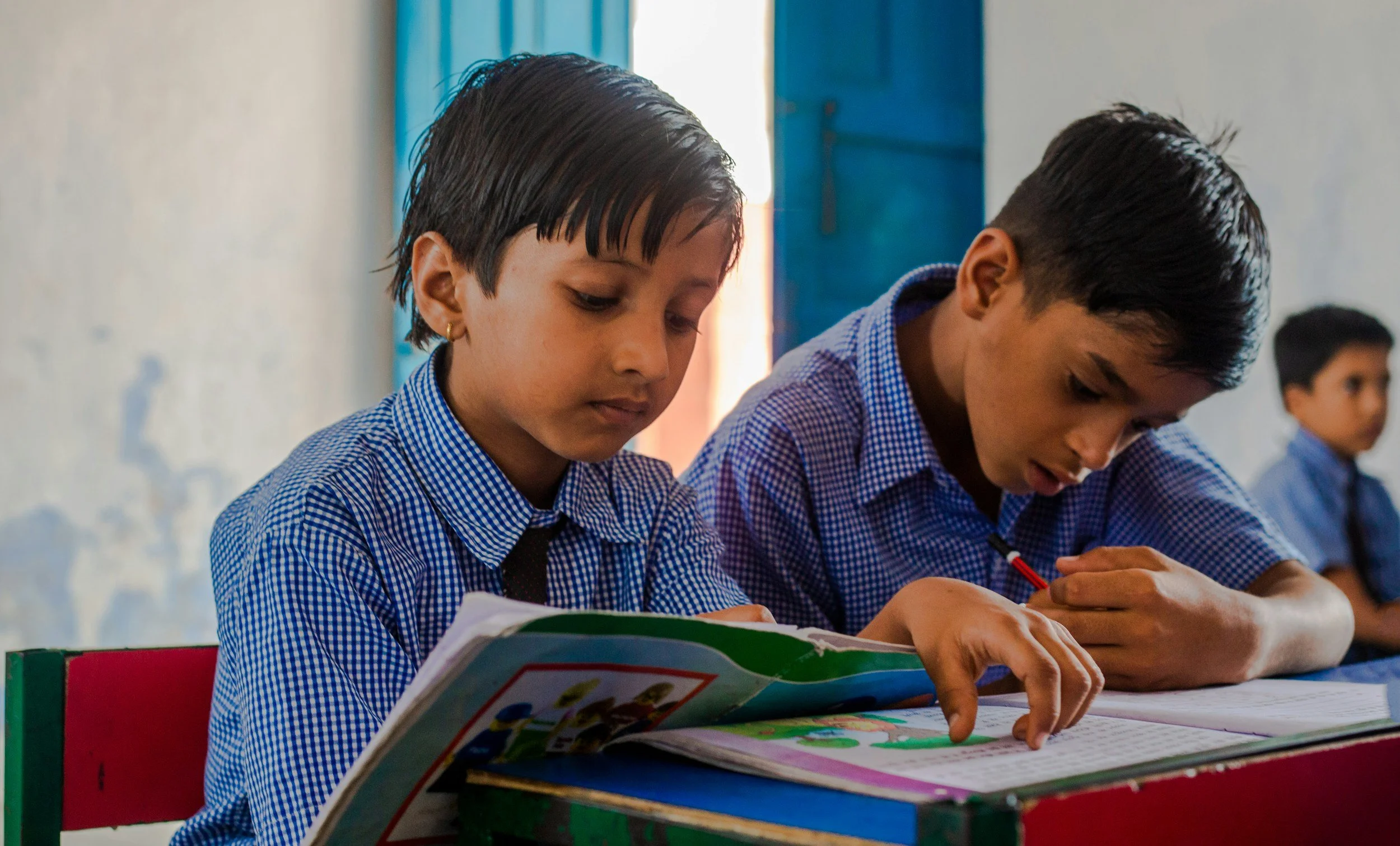 Students in school uniforms sitting at desks, reading books in a classroom.
