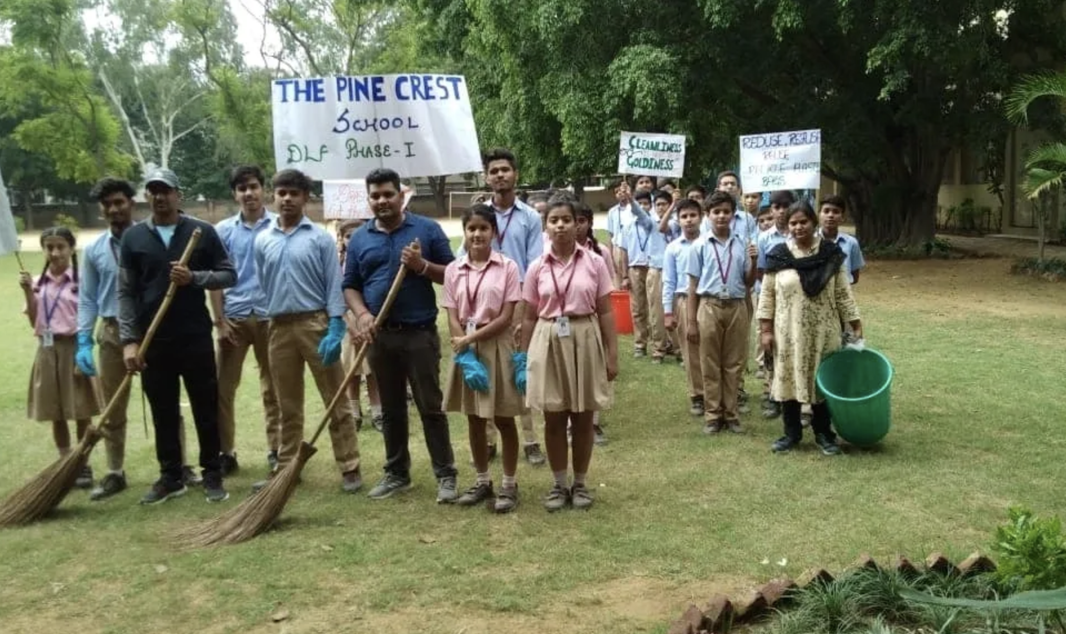 Group of students and teachers outdoors holding signs about environmental conservation and cleaning activities at a school.