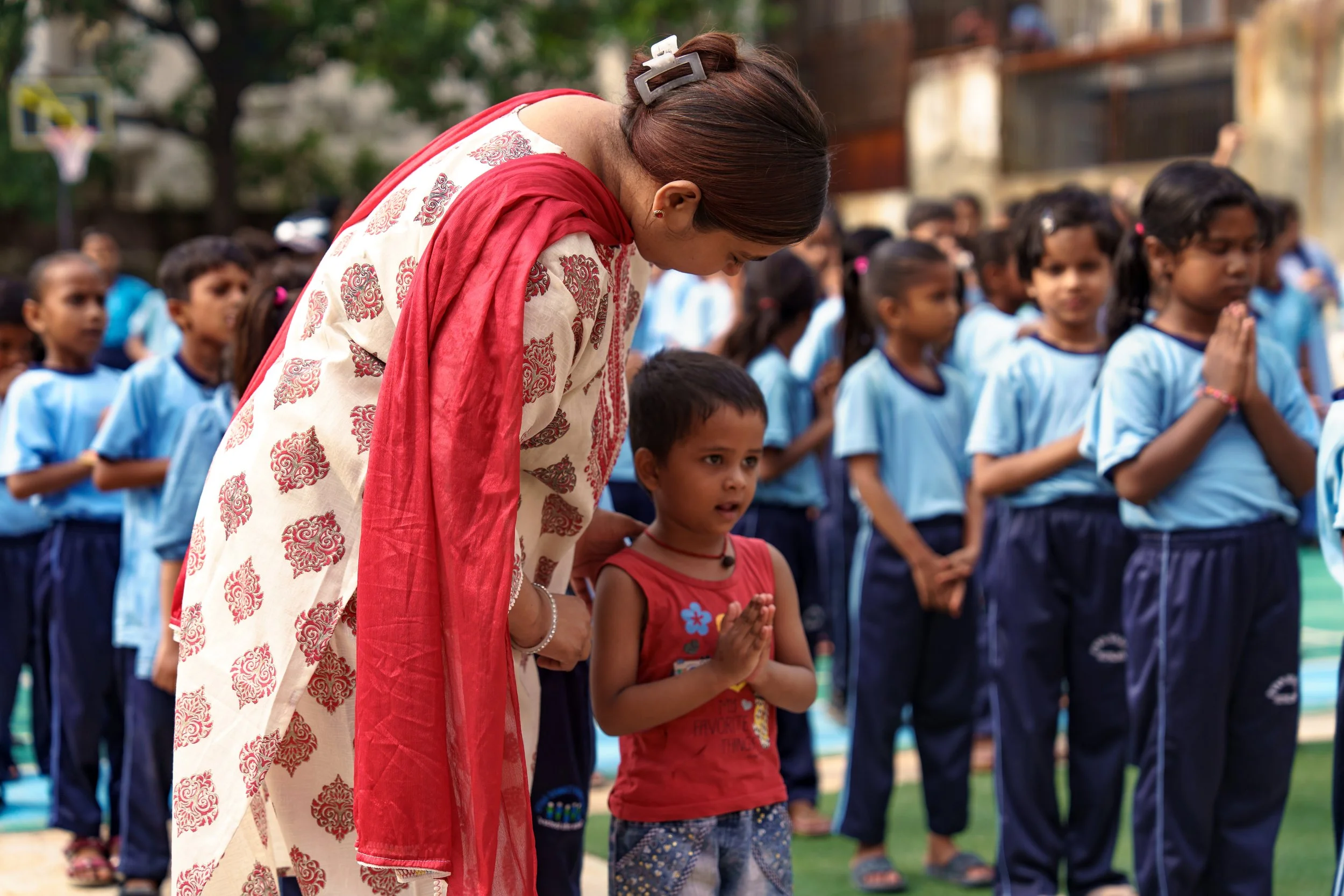 A woman wearing a white and red traditional dress and a hair clip is praying with children, who are also praying, at an outdoor event.