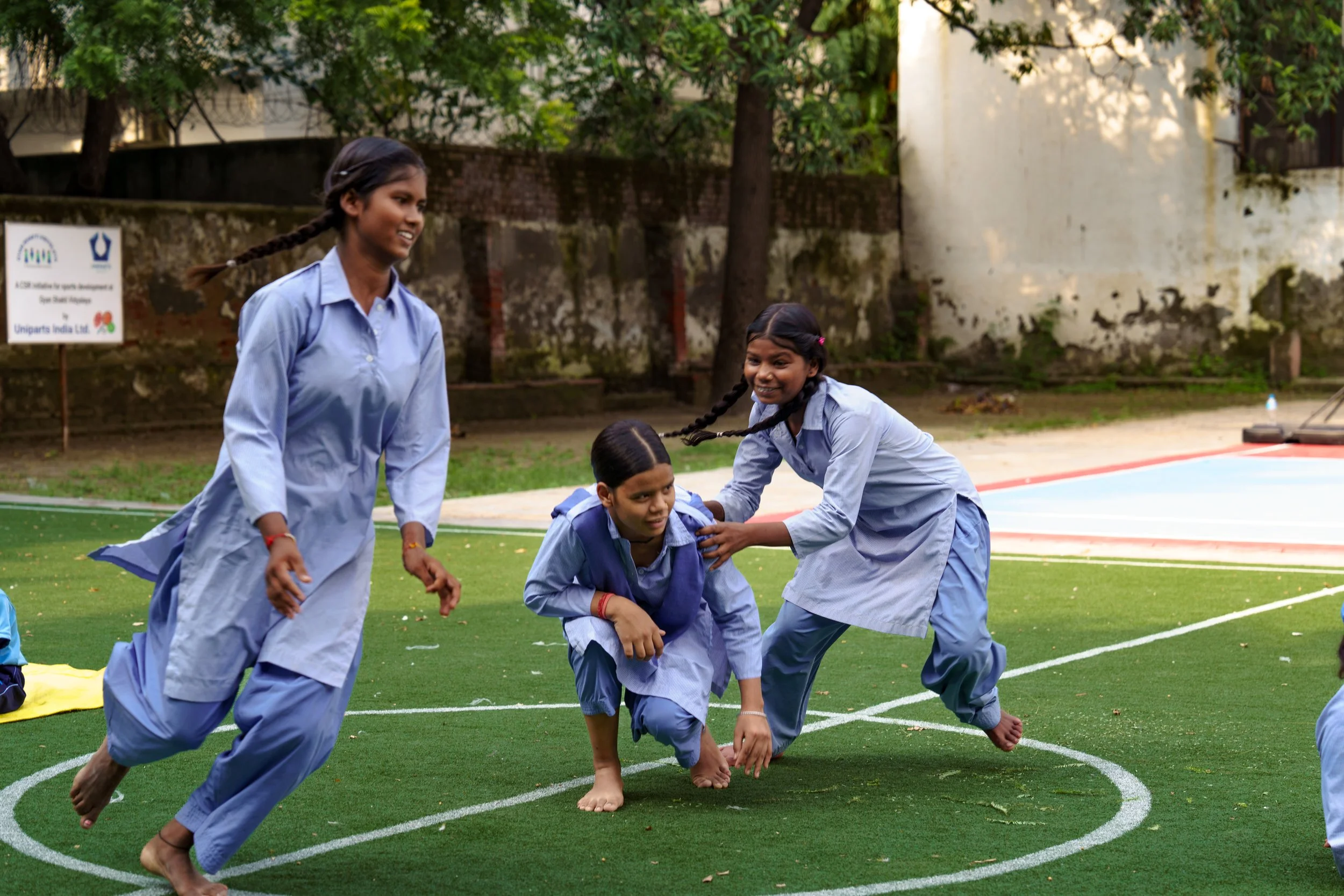Group of young girls in school uniforms playing a game or sport outdoors on a green field