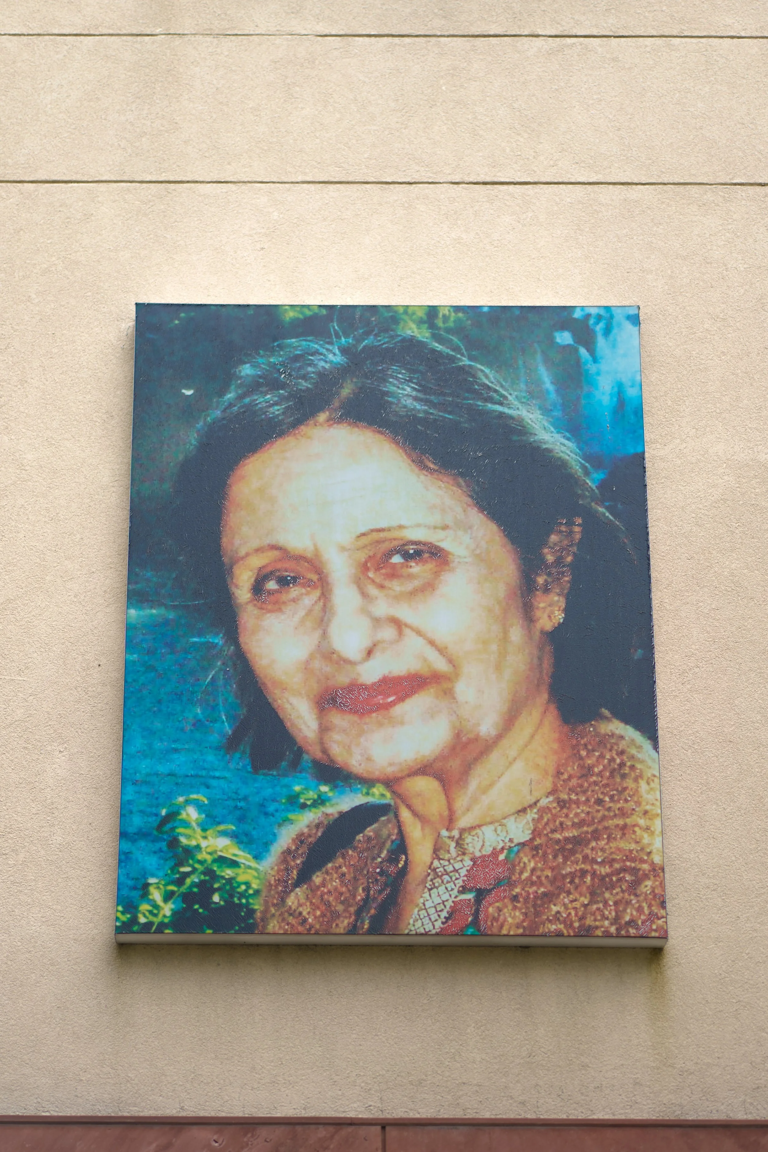 A close-up of a portrait photograph of an elderly woman with dark hair, wearing traditional clothing, on a beige wall.
