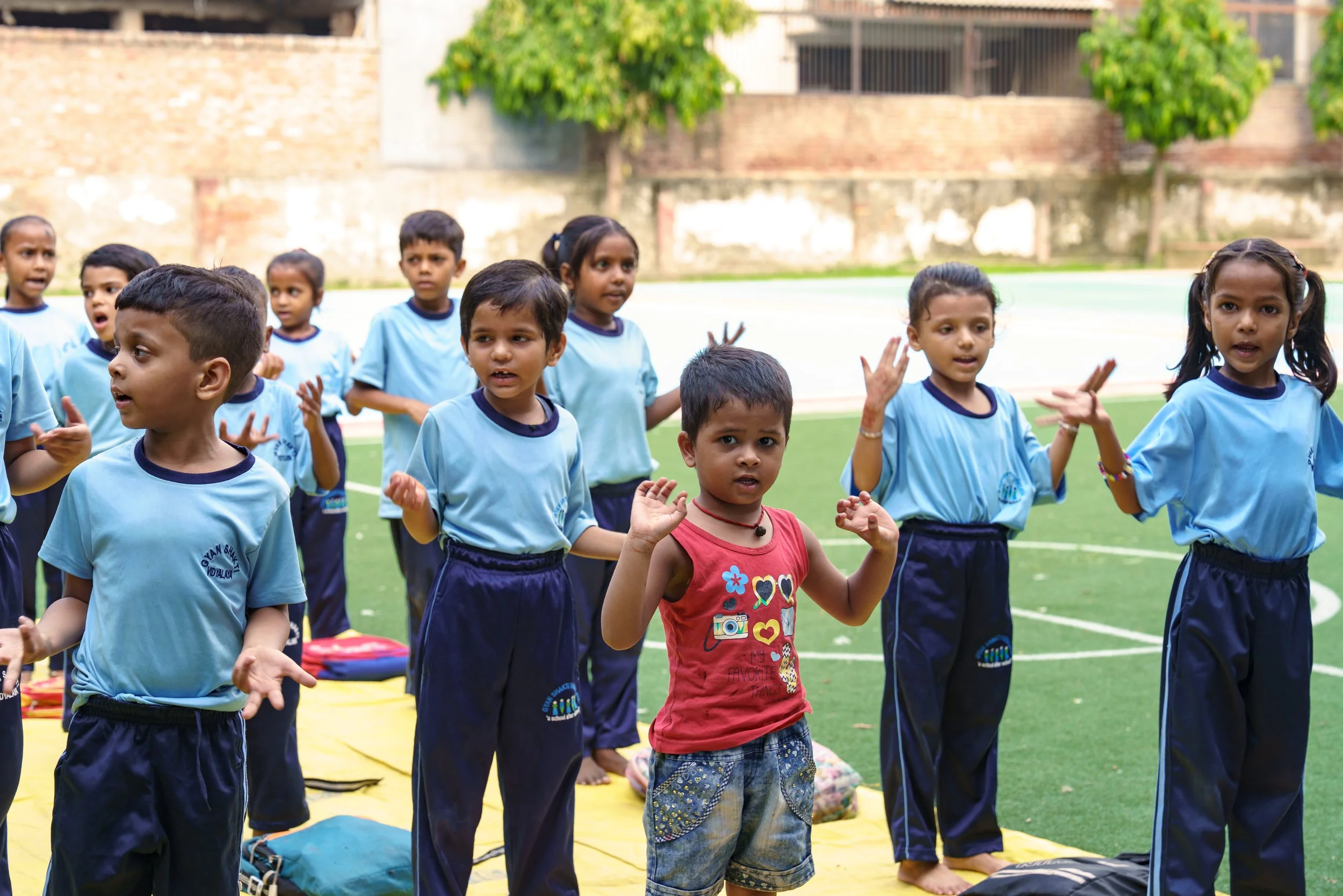 Group of young children in blue school uniforms standing outdoors on a sports field, engaging in an activity.