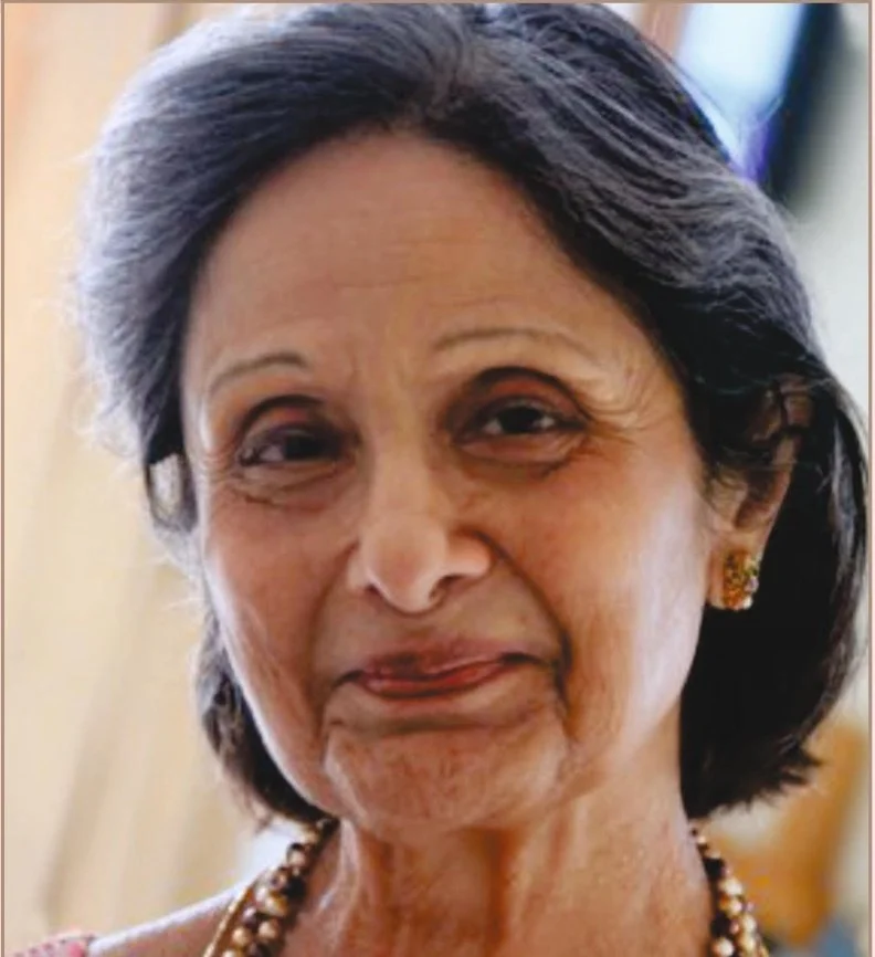 Close-up of an older woman with short, dark hair, smiling warmly, wearing earrings and a necklace.