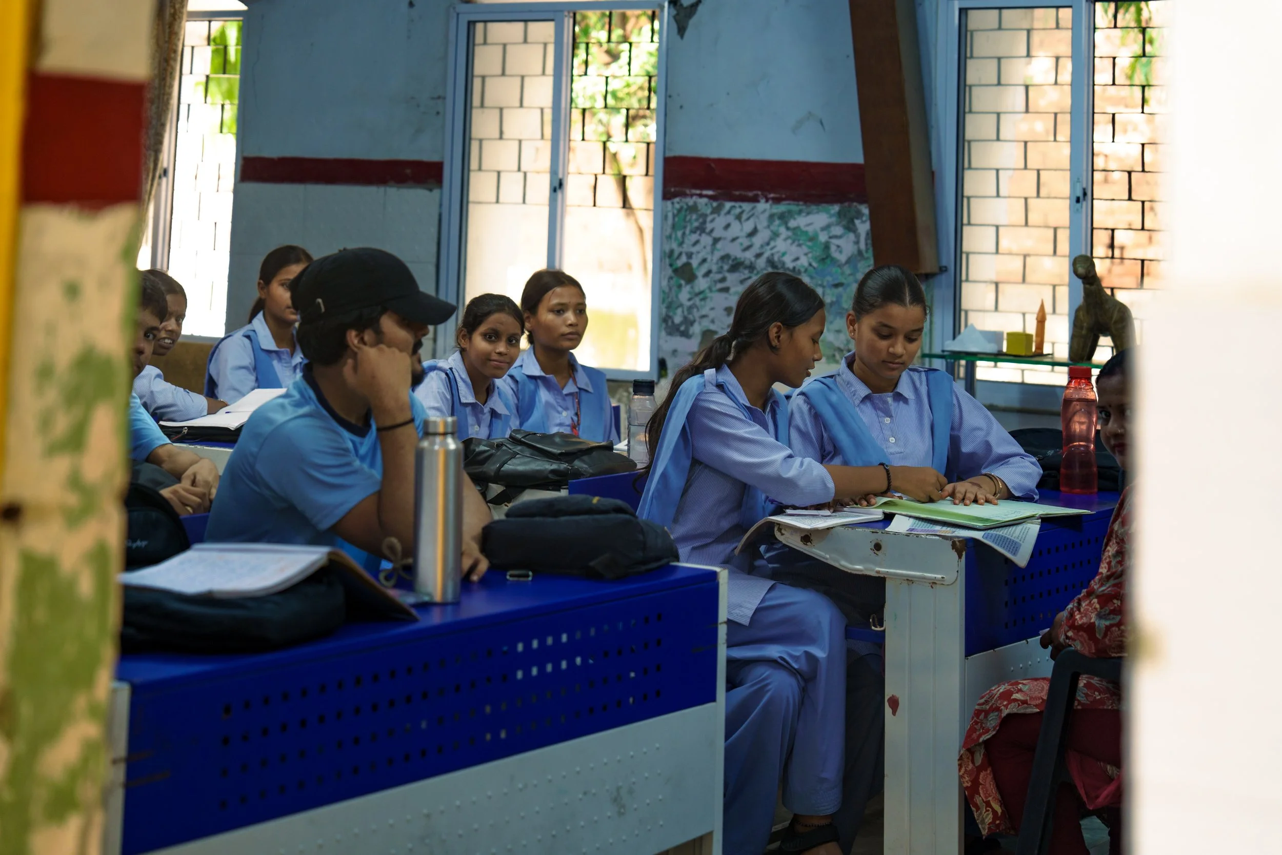 Students in uniform sitting at desks inside a classroom, engaged in lesson or discussion.