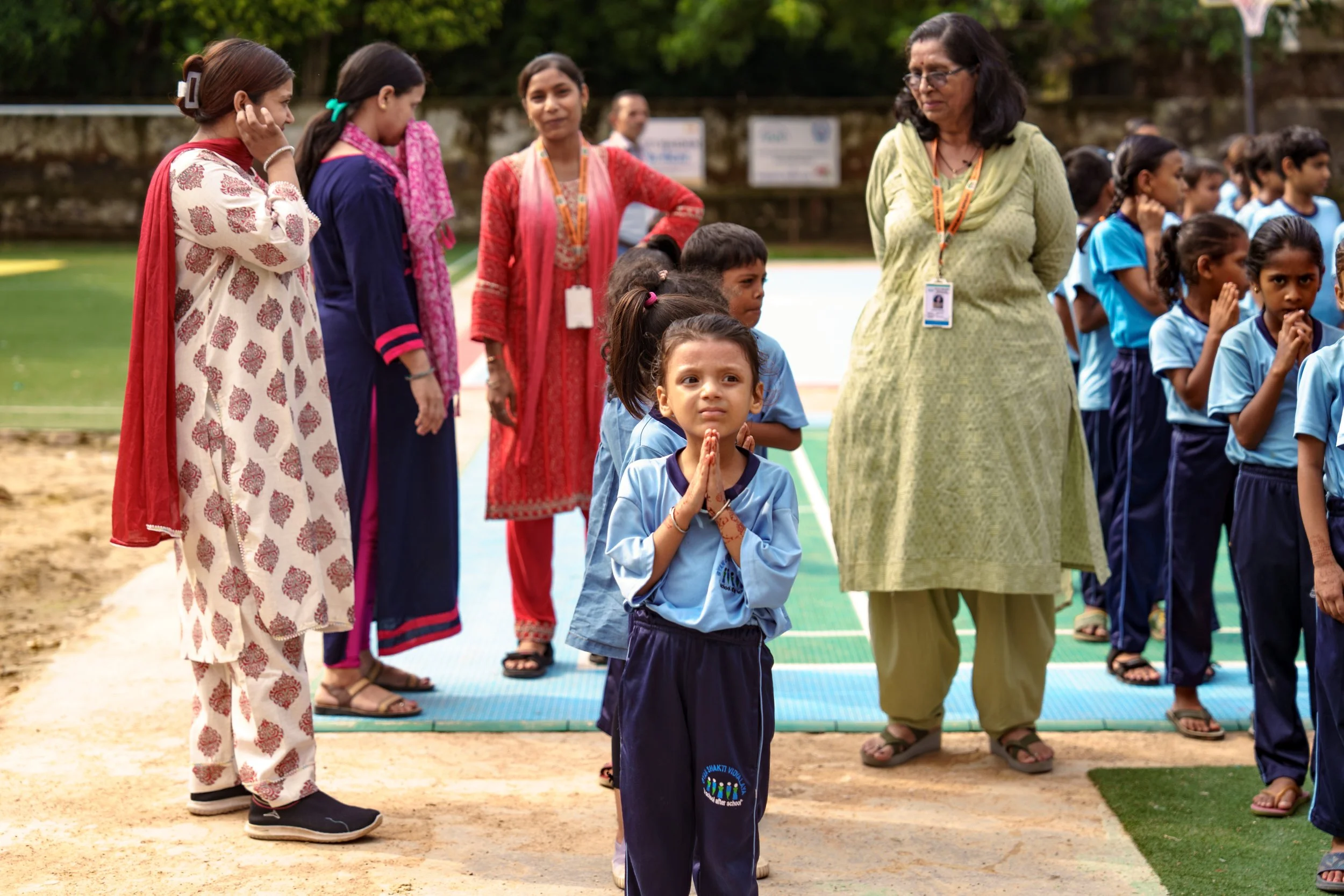 A group of school children and women standing on a sports field, participating in an outdoor activity or ceremony.