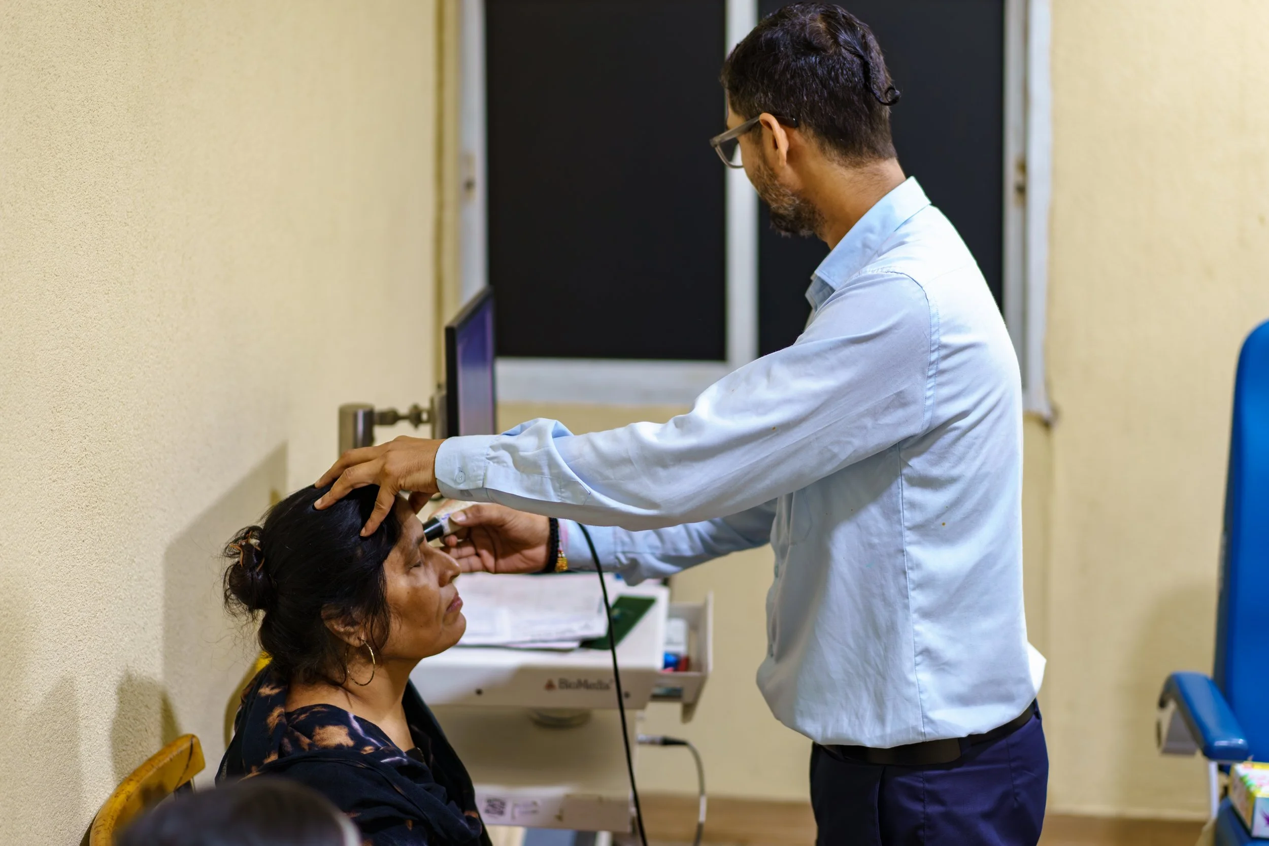 A healthcare professional using a stethoscope to examine a patient in a clinic or hospital setting.