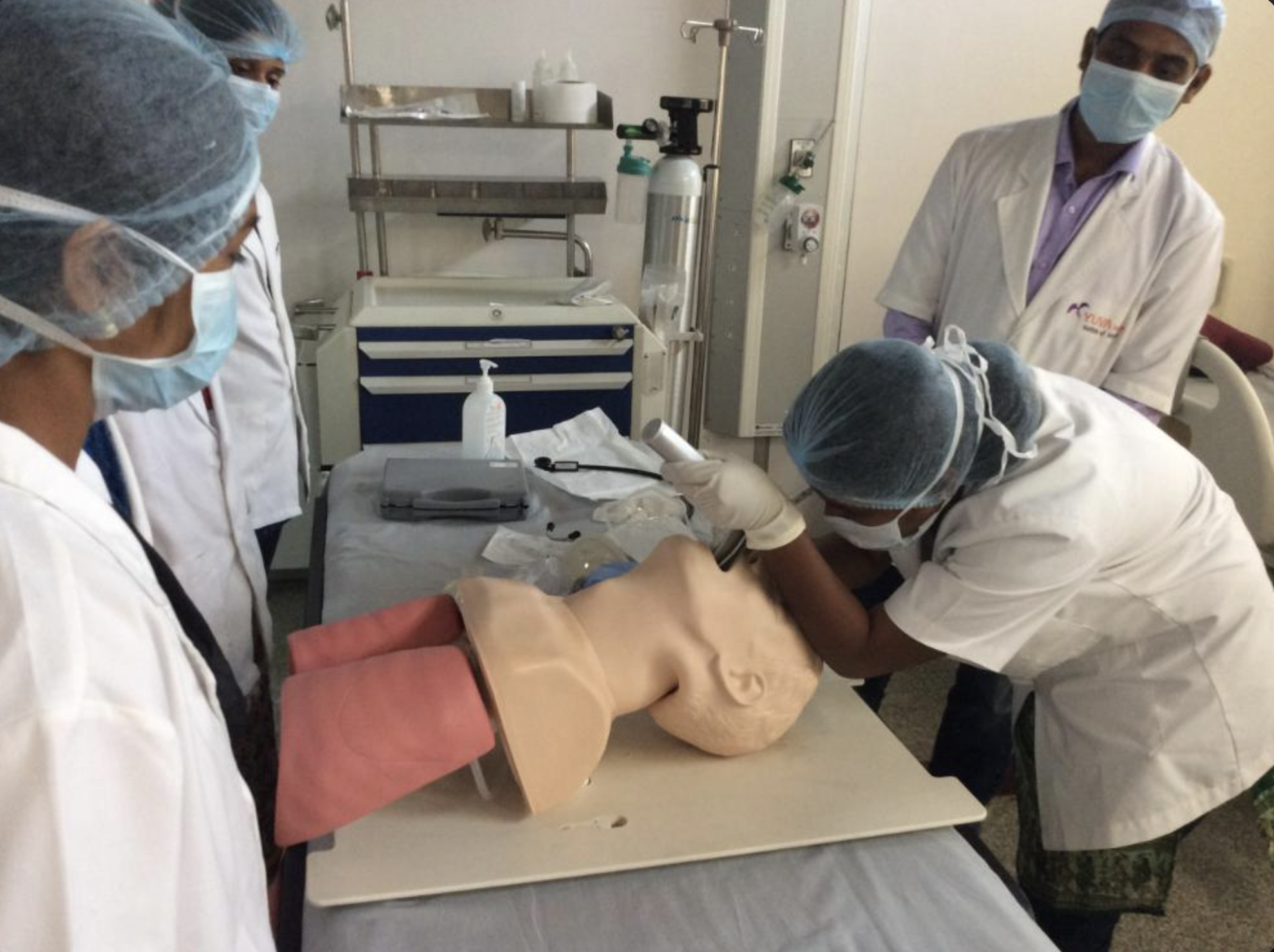 Medical professionals in masks and scrubs attending to a patient on a bed in a hospital room.