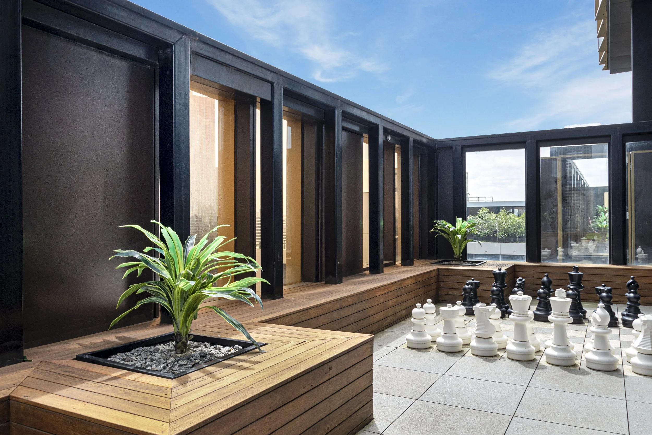 Rooftop communal space with timber seatings and unroofed skylight, on the side is a chess to play with.