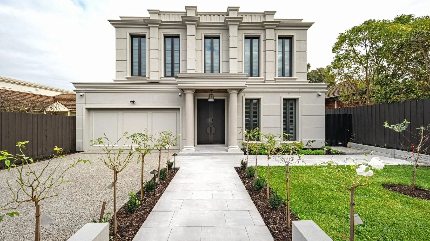 The front of a mansion, with a garden with two strips of garden bed alongside the entrance walkway.