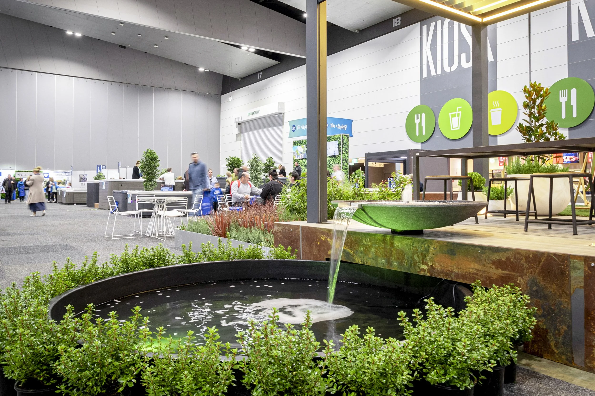 Indoor public space with plants, seating areas, and large icons indicating dining, drinking, and seating areas on a wall.
