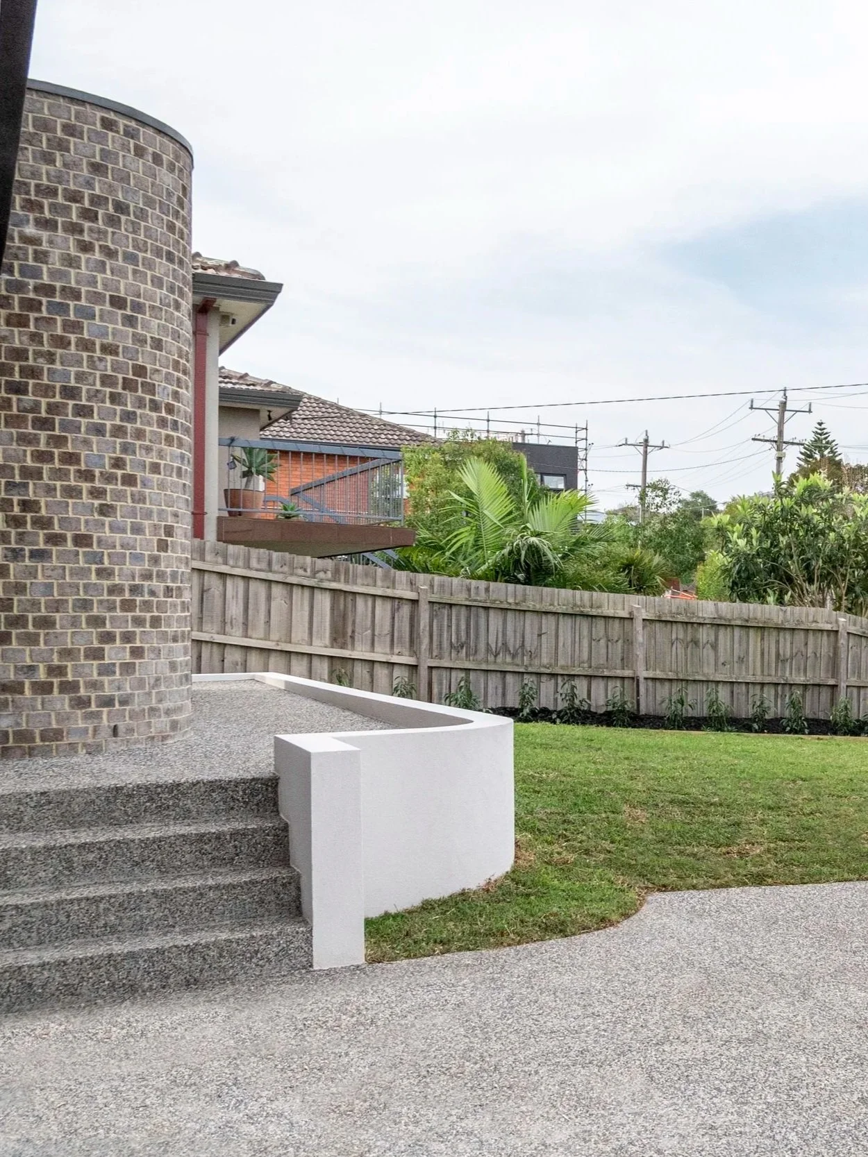 The white wall matches with the grey exposed aggregate concrete driveway, creating level difference with the lawn below.