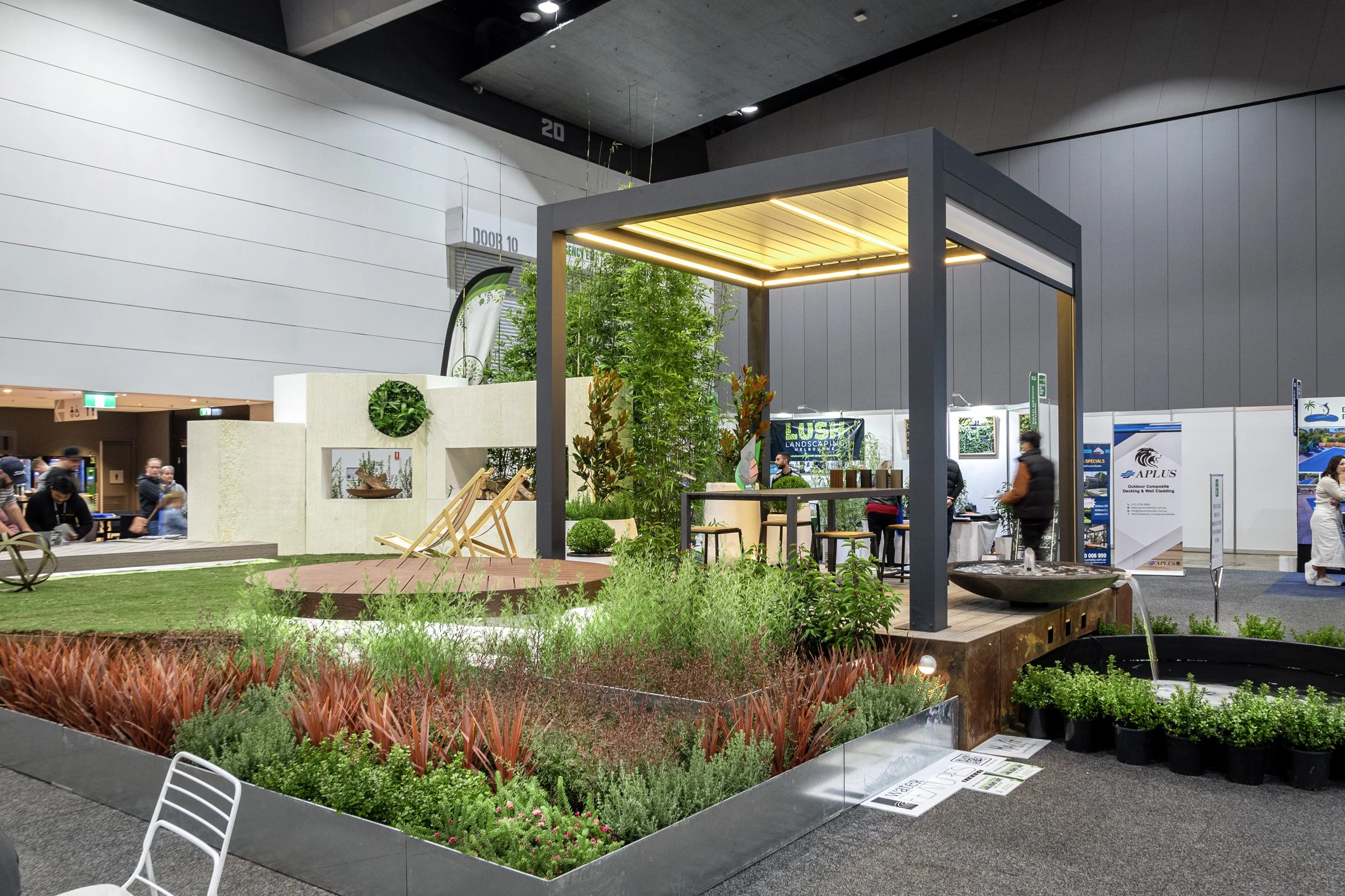A modern pergola on timber deck, with lawn and diverse plantation and water feature.