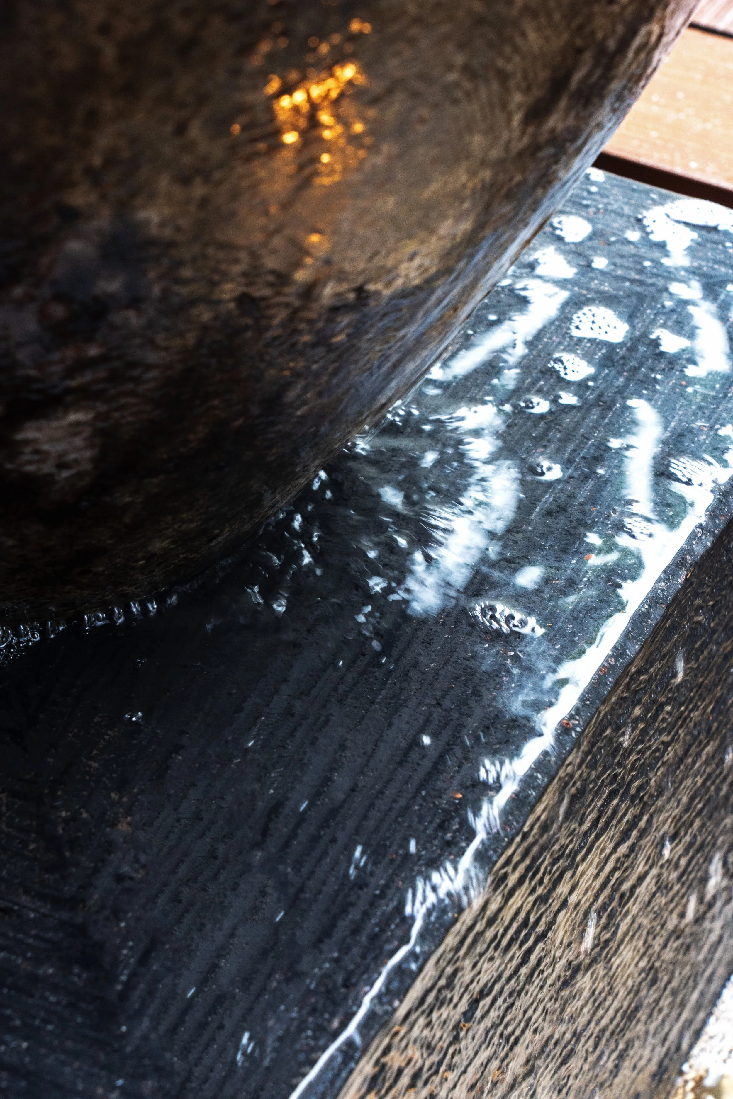 Close-up of water flowing over black stone or concrete with reflections and bubbles