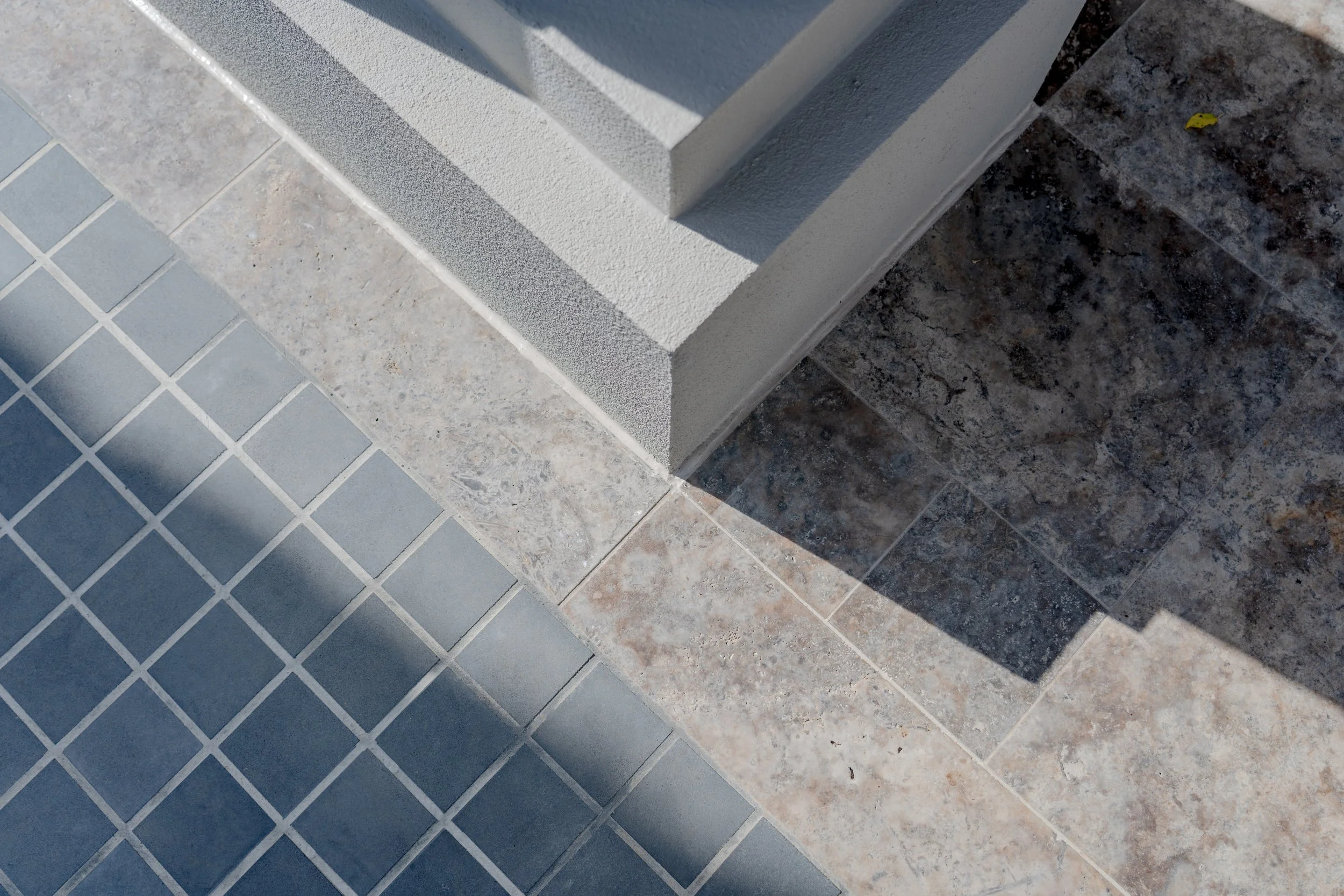 Close-up of a corner with different types of tiles and textured wall at the base.
