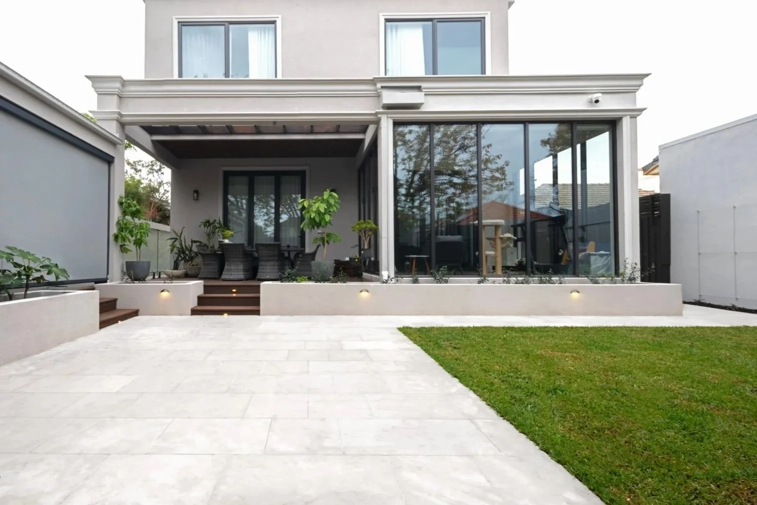 The backyard garden with a elevated outdoor entertainment deck and a lawn which is able to be overlooked from inside of the house. White pavings are to match with the architecture.