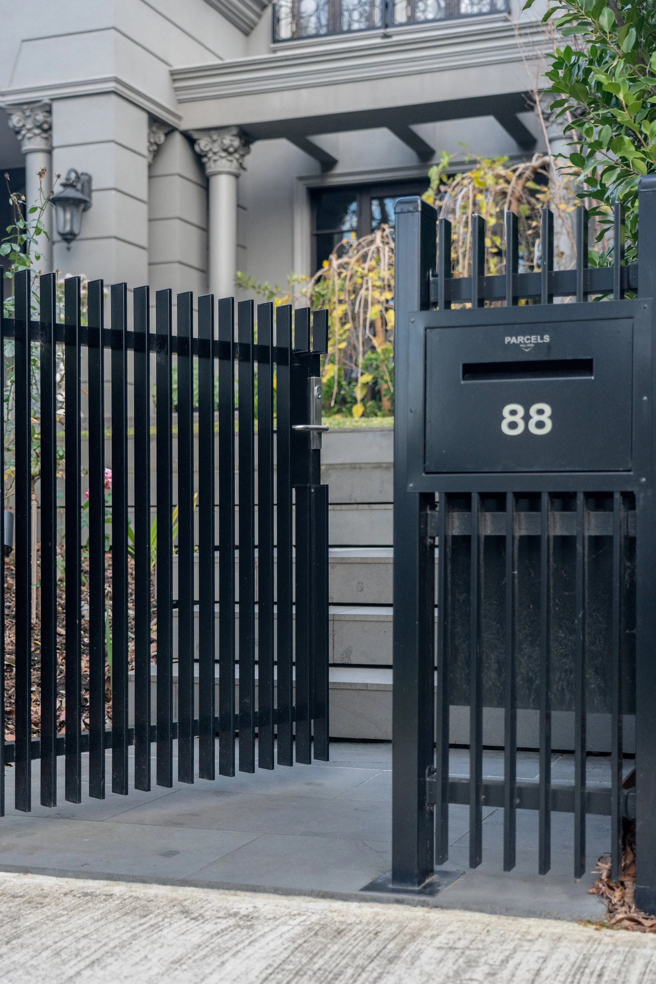 Black metal gate in front of a modern residential building with stairs and greenery.