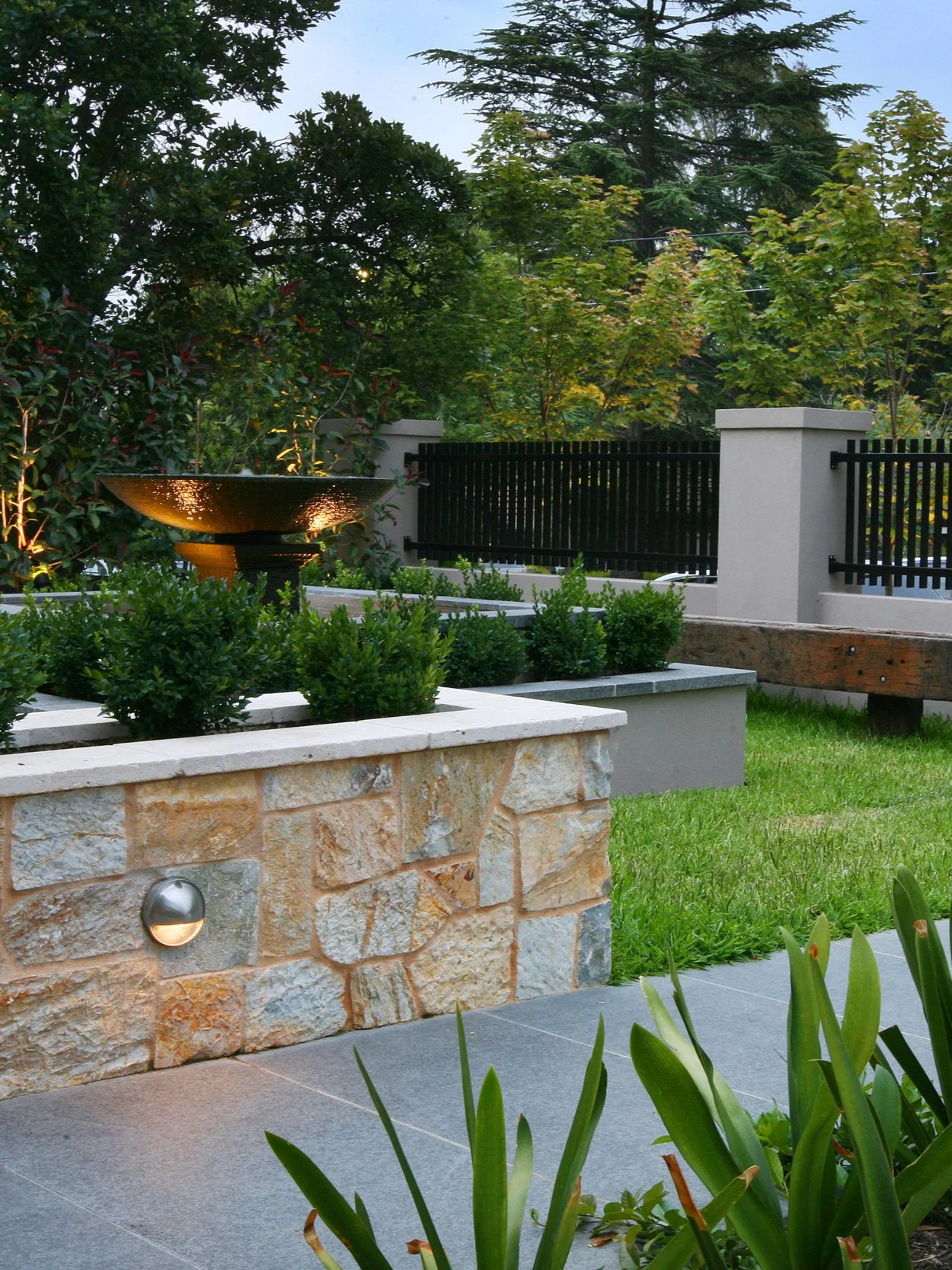 The classic water fountain feature with bluestone capping and vegetation below it, and the side limestone dwarf wall matches the classic feeling of garden design.