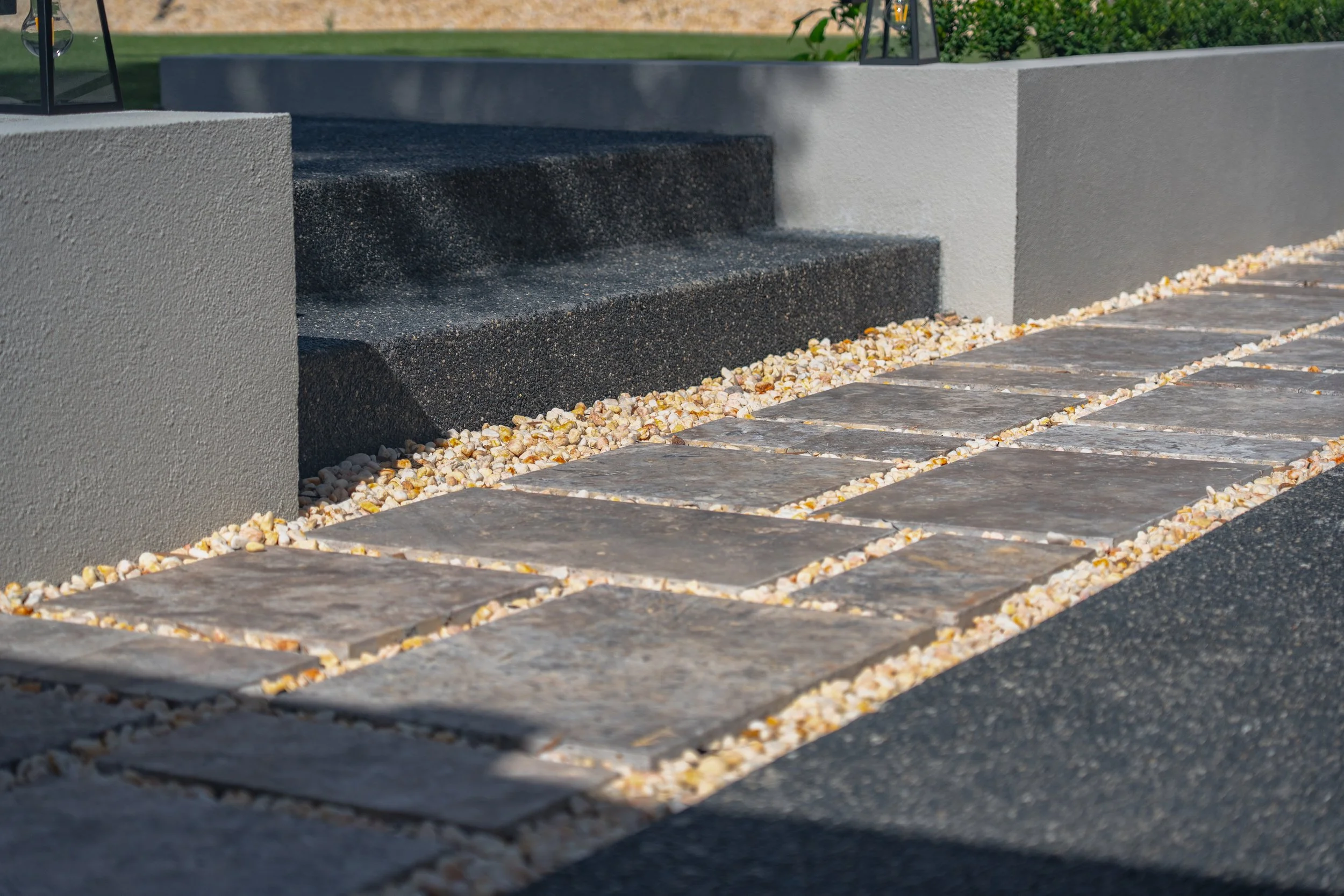 The loosely packed bluestone paving steps with selected rocks and pebbles infill, creating interesting layering with the exposed aggregate concrete and leveled lawn.