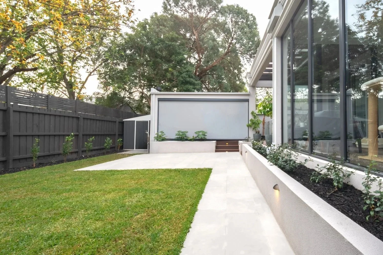 The backyard area is a large open multi-functional space with lawn and white stone pavings.