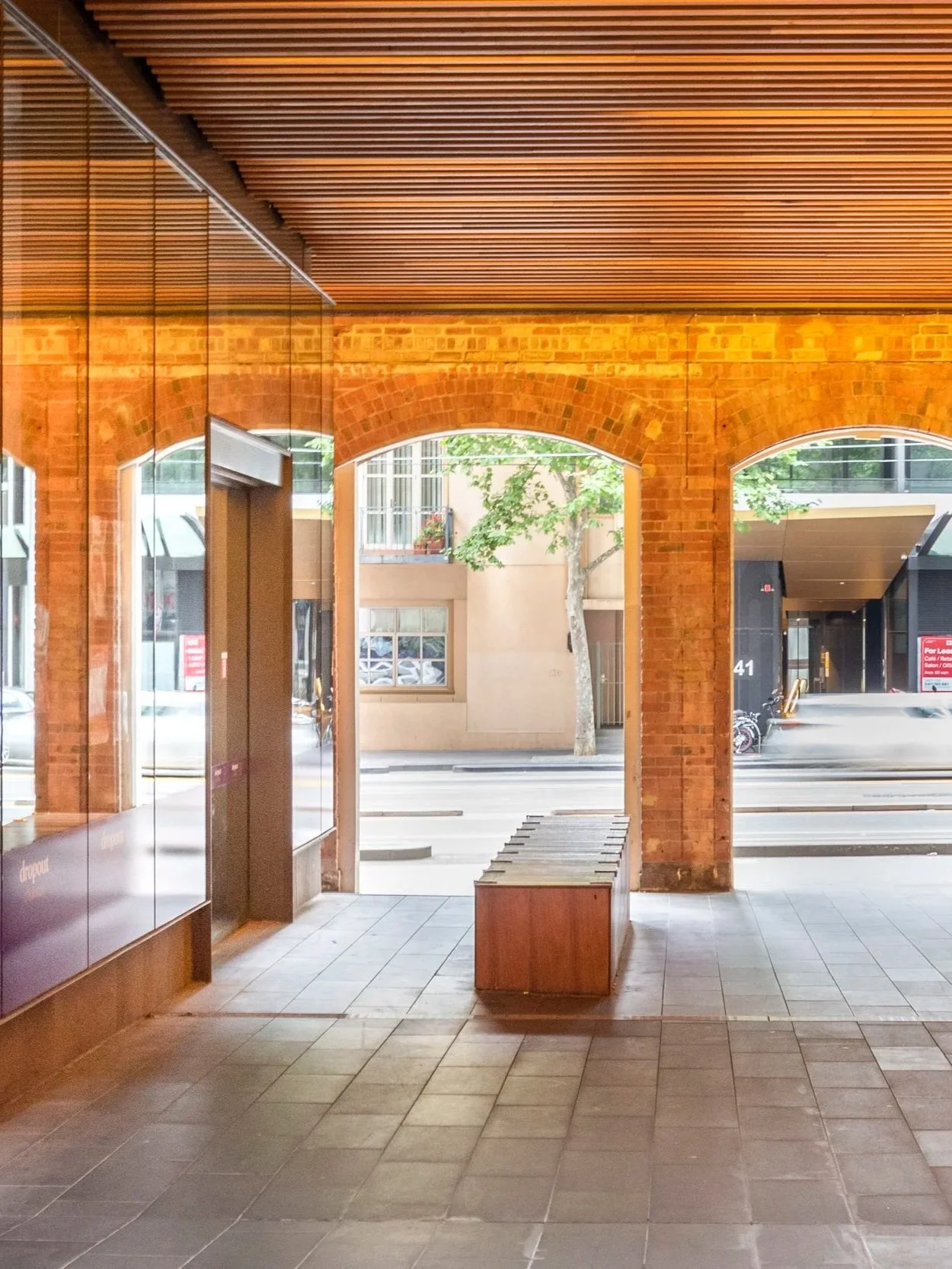 The arches on the exit to the busy street create a semi-enclosed space, capturing the yellow environmental light and the reflection on the architecture's glass facade.