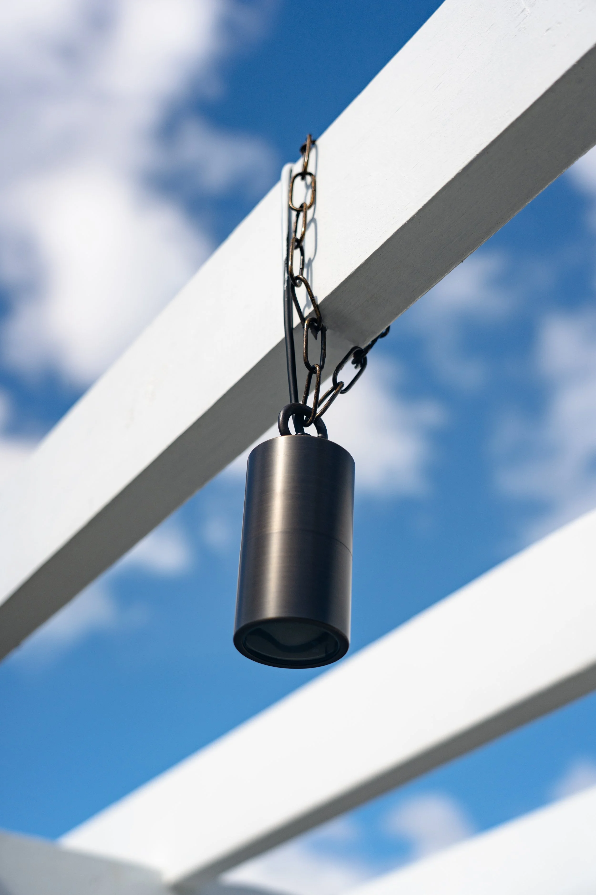 A wind chime hanging from a white wooden structure with a blue sky and some clouds in the background.