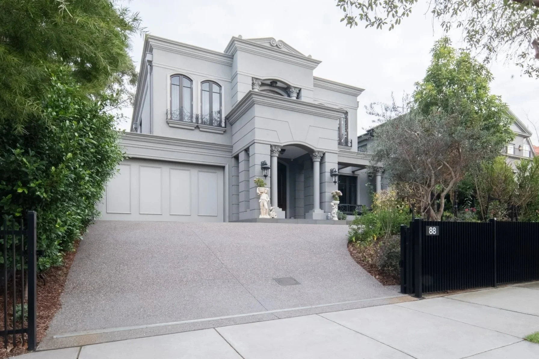 A gentle slope going up the driveway, reaching the modern french design architecture, with elegant garden design in front.